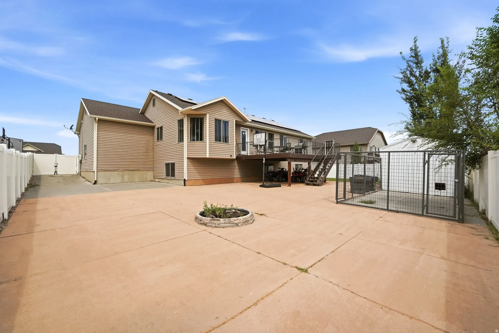 Expansive concrete patio area featuring a stone-ringed planter, white vinyl fencing, and a large multi-level deck with stairs