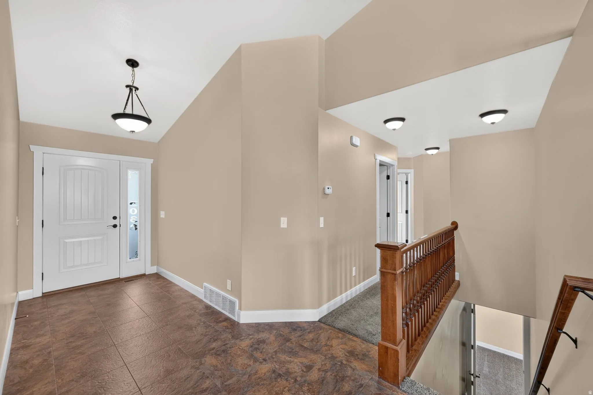 Front entry featuring a paneled door with a sidelight, tiled flooring, vaulted ceiling, and a contemporary pendant light