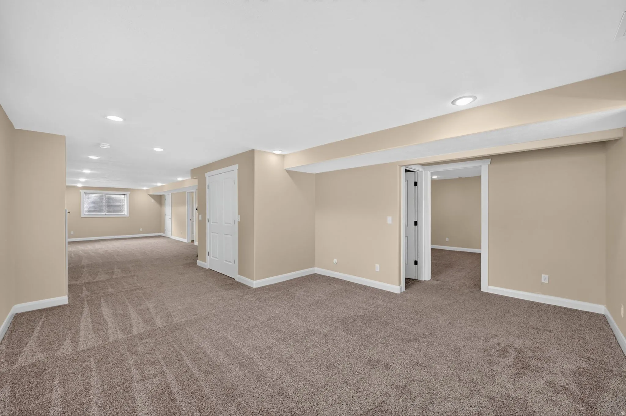 Spacious carpeted room featuring recessed lighting, a neutral color palette, white trim, and multiple doorways