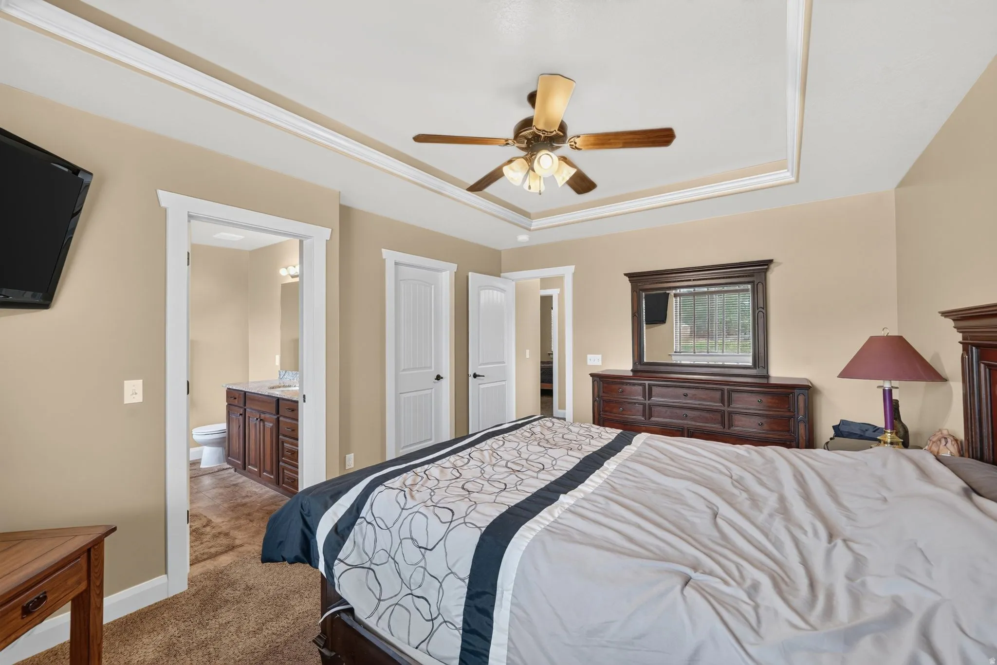Recessed tray ceiling with crown molding, ceiling fan, and warm-toned wall paint