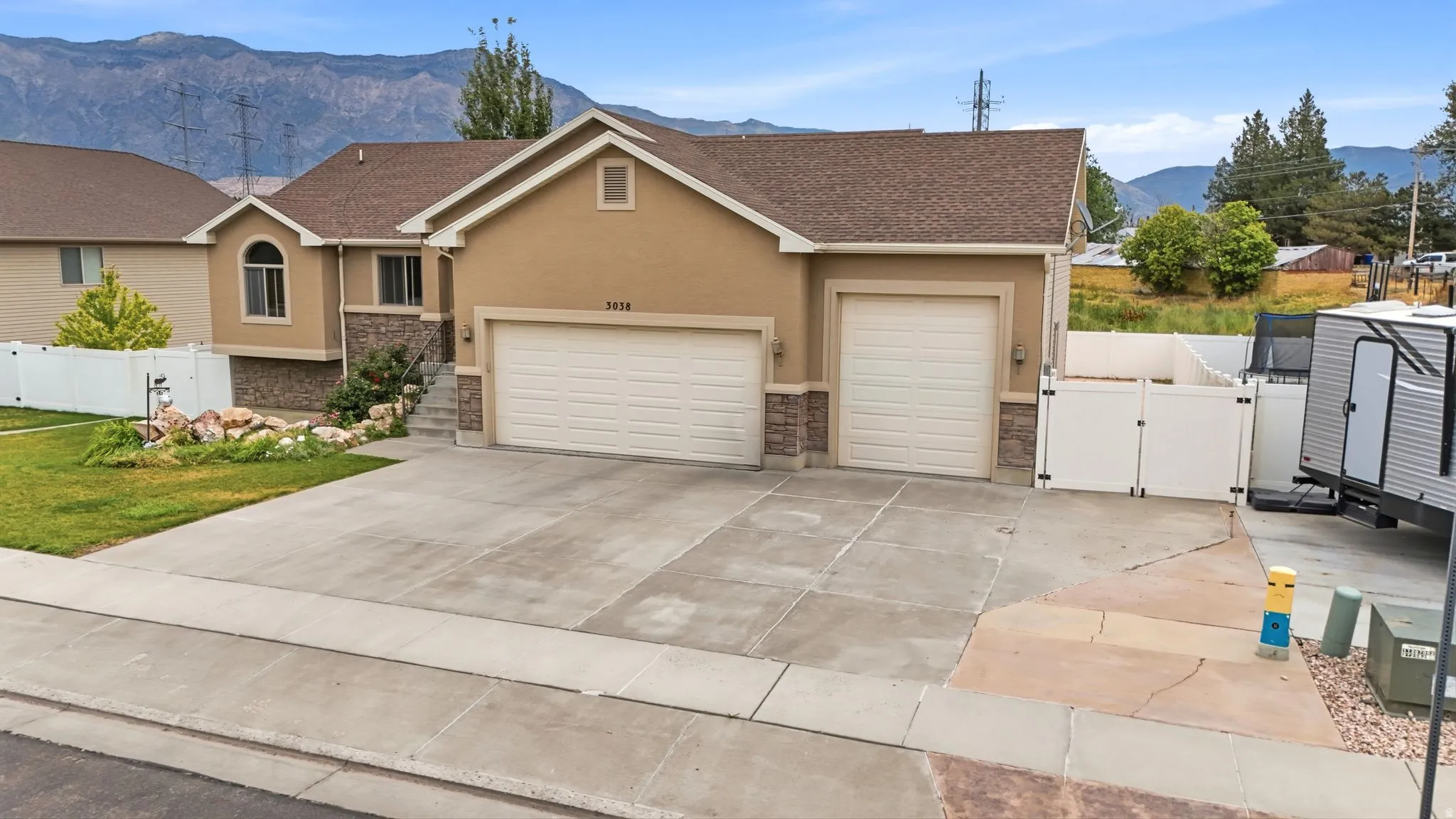 Contemporary stucco and stone exterior featuring a two-car garage, an additional single-car garage, and a concrete driveway
