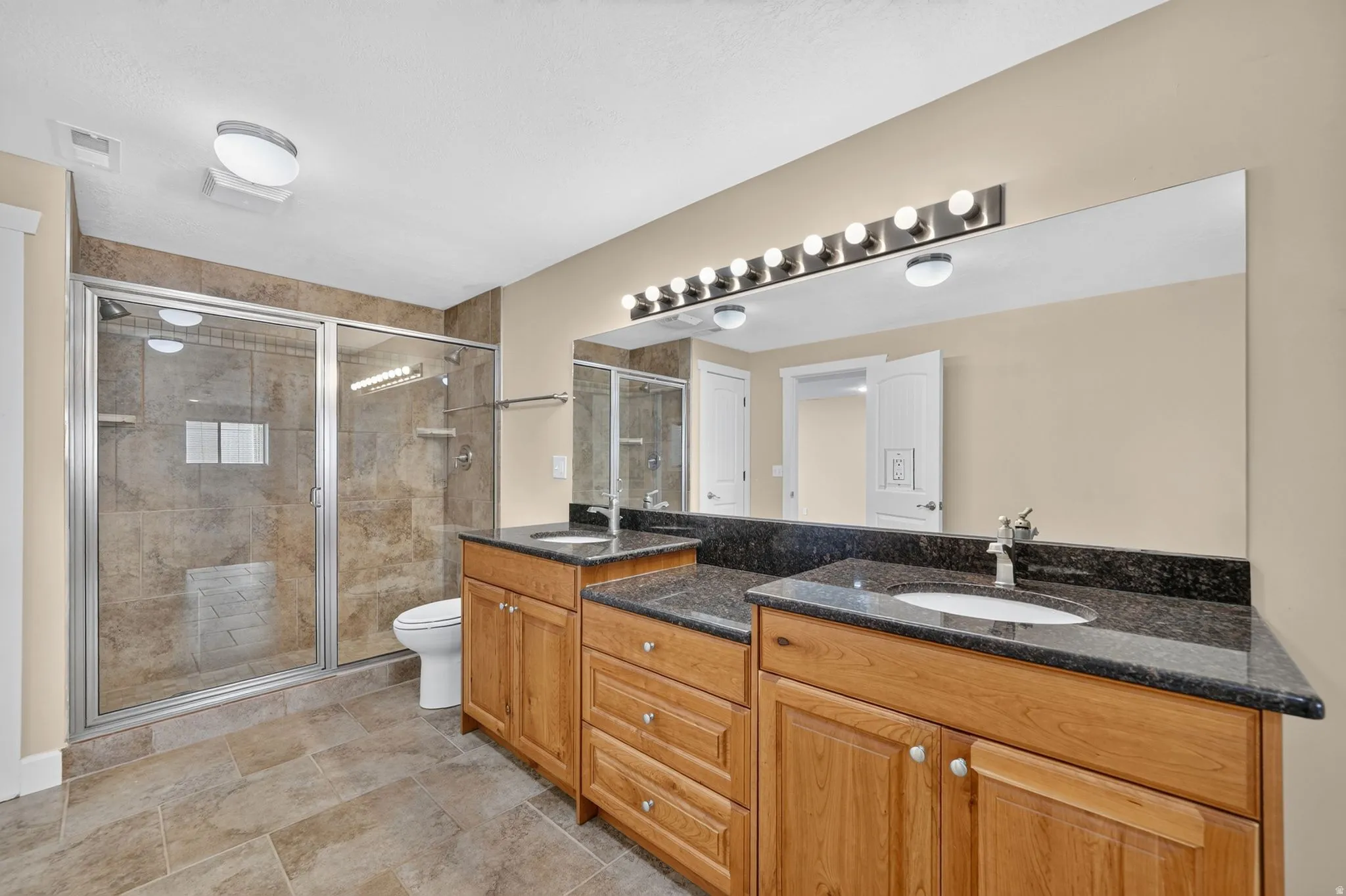 Dual sink vanity with dark stone countertops and wood cabinetry