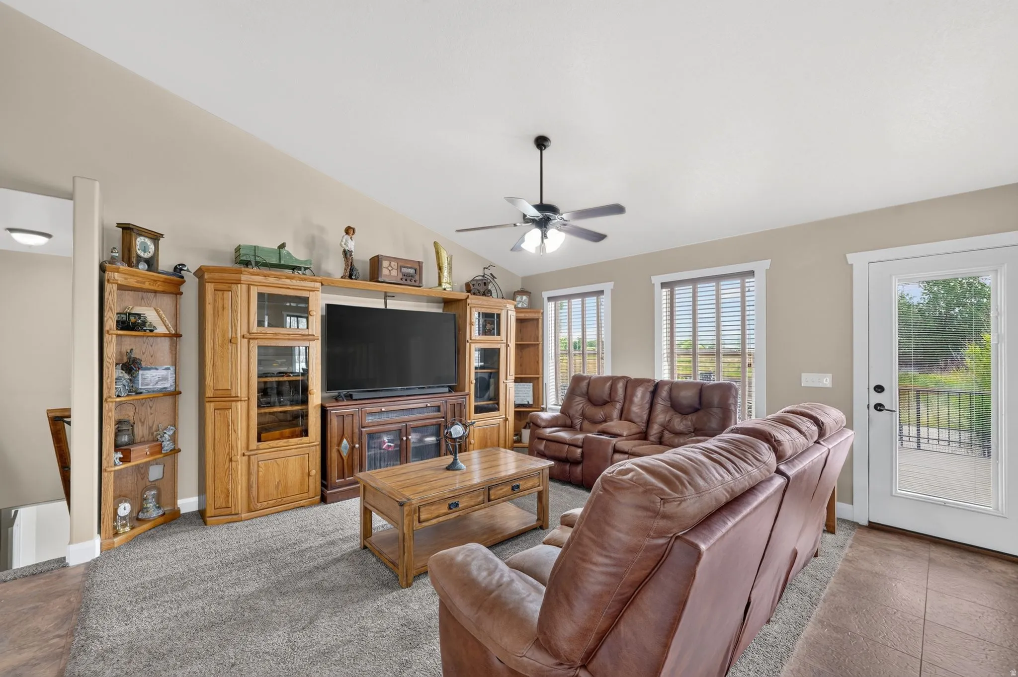 Living area featuring a vaulted ceiling with a ceiling fan, carpet flooring, and a glass-paned door opening onto an outdoor deck