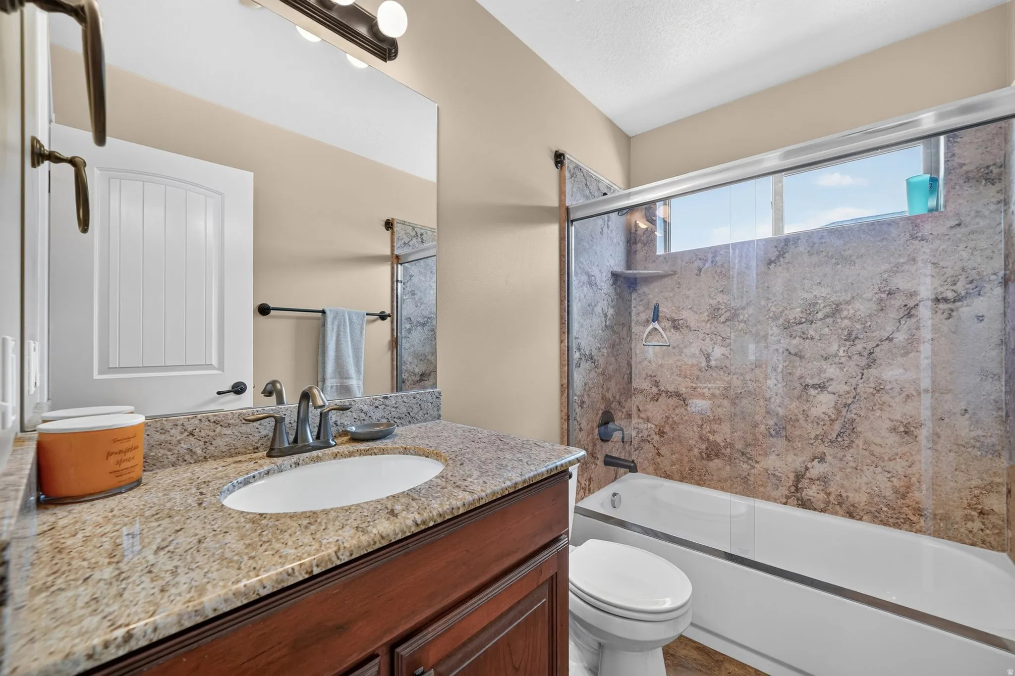 Bathroom featuring a granite countertop vanity with an undermount sink, a tub/shower combination with stone-look wall surrounds, and a transom window