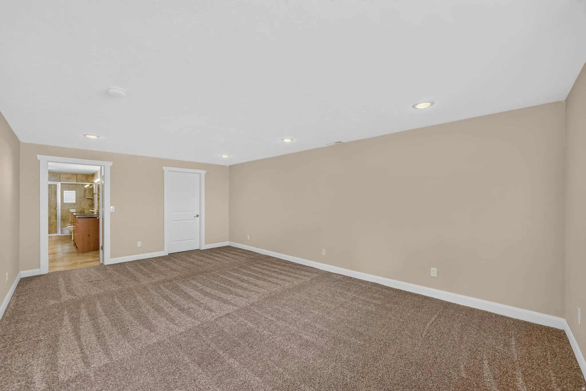 Spacious room with plush carpeting, recessed lighting, neutral wall tones, and white trim