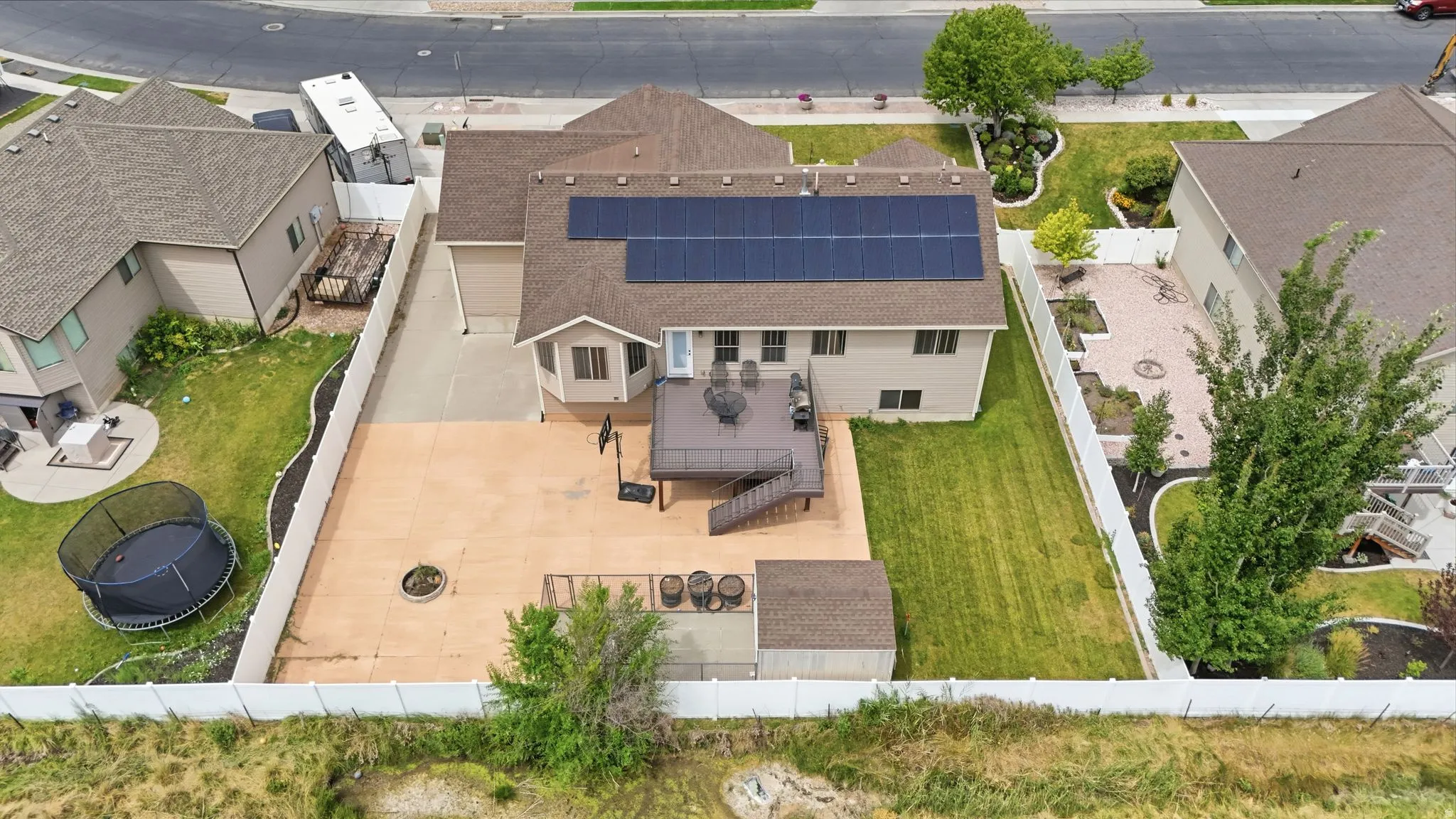 Rear exterior featuring a spacious concrete patio, multi-level wood deck, solar panels, and a white vinyl fence