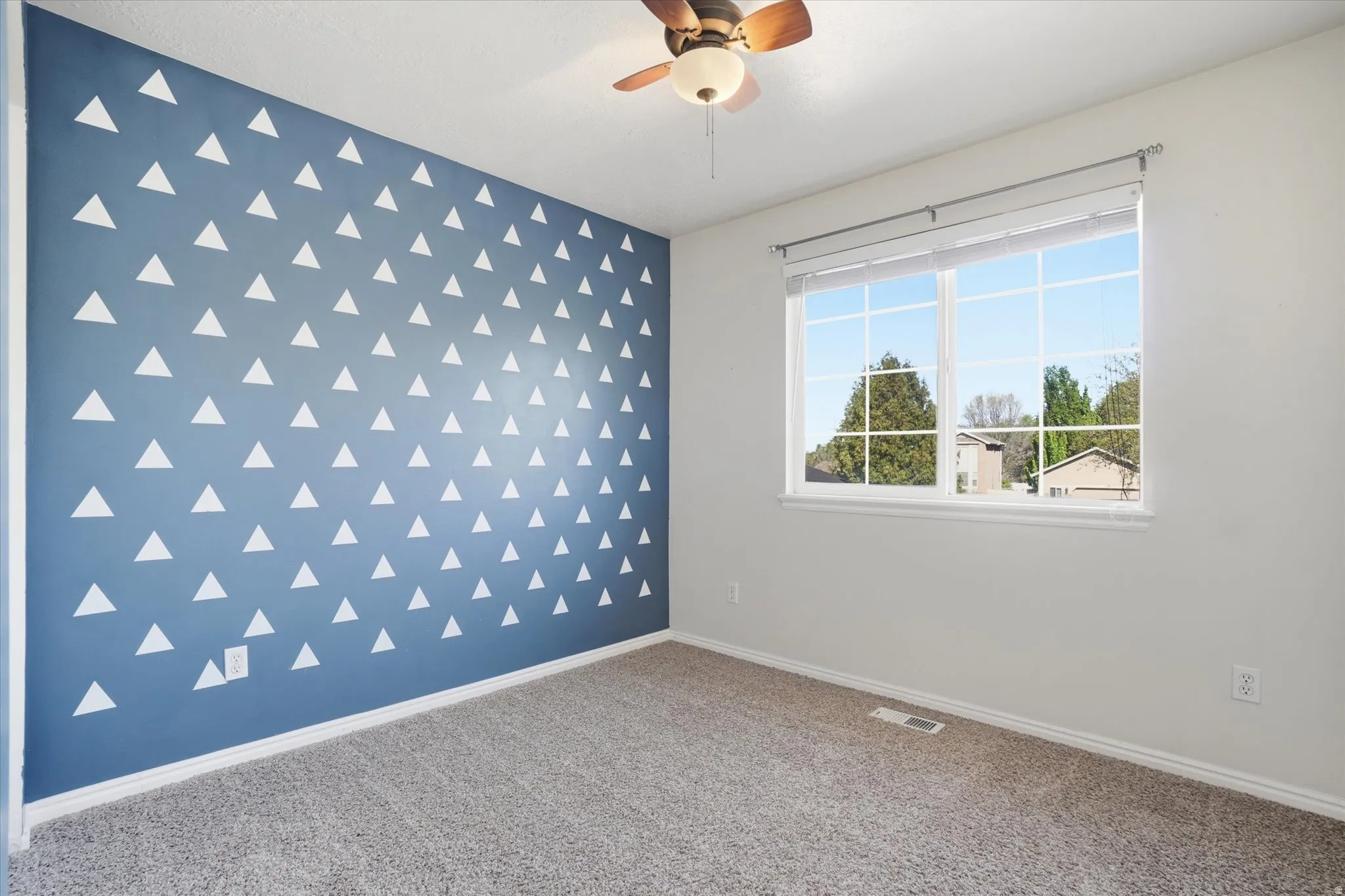 Carpeted empty room featuring an accent wall and a ceiling fan