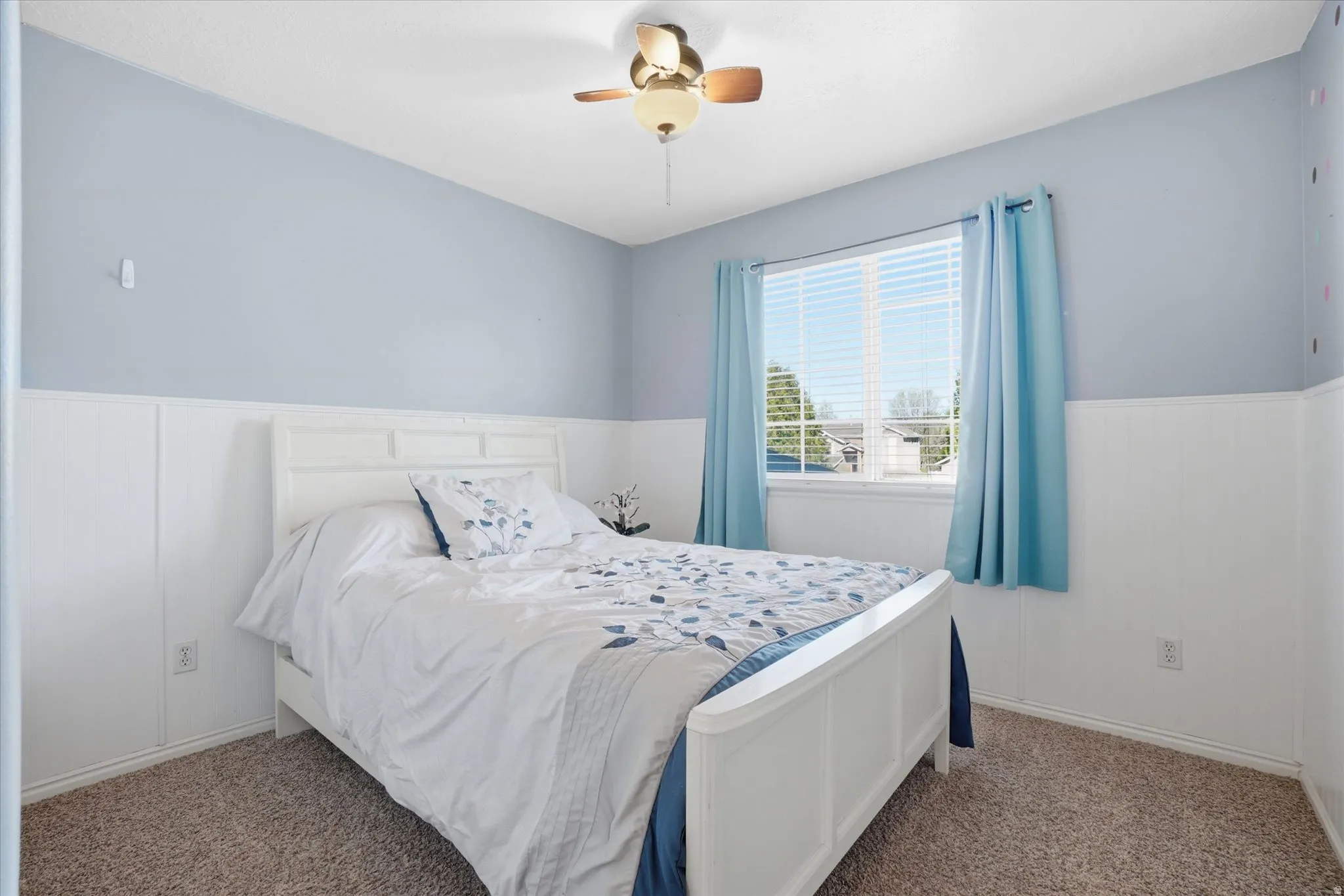 Carpeted bedroom with wainscoting, a ceiling fan, and a decorative wall