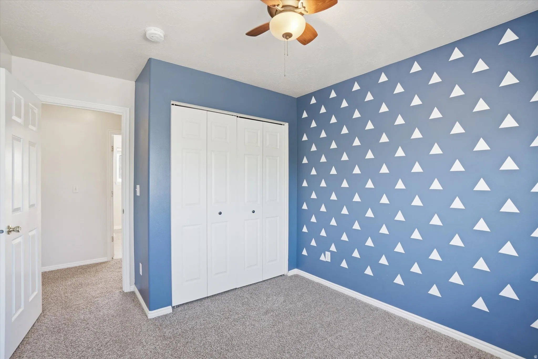 Unfurnished bedroom featuring carpet, an accent wall, a closet, and a ceiling fan