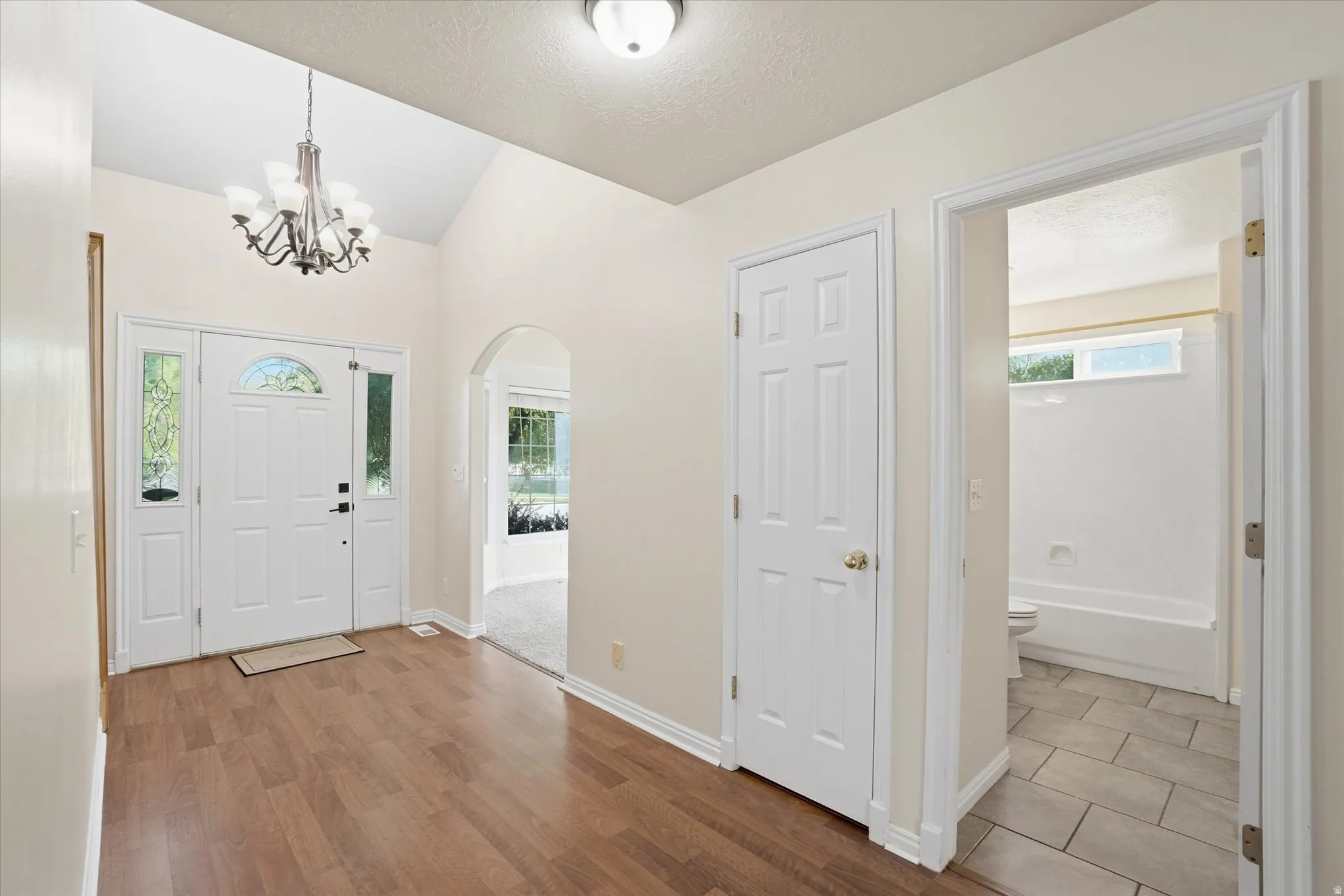 Foyer with arched walkways, light wood-type flooring, and a chandelier
