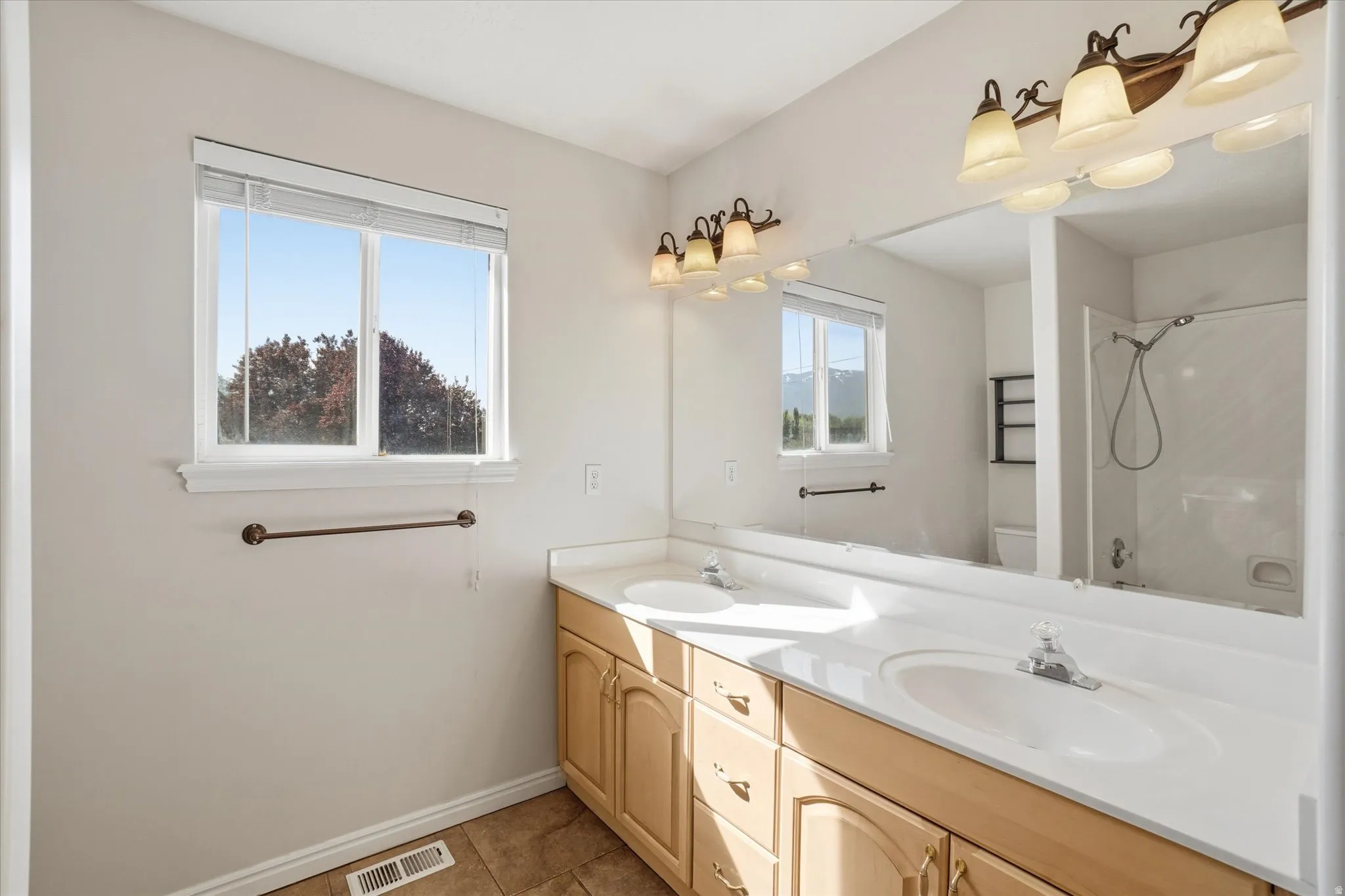 Full bathroom featuring double vanity, light tile patterned floors, and a shower