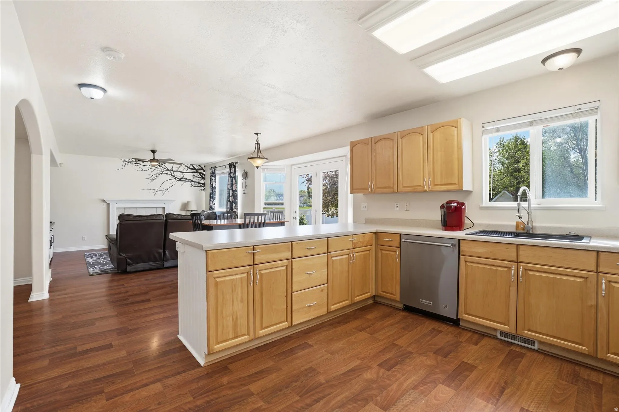 Kitchen with light wood finish cabinets, dishwasher, a fireplace, light countertops, and open floor plan