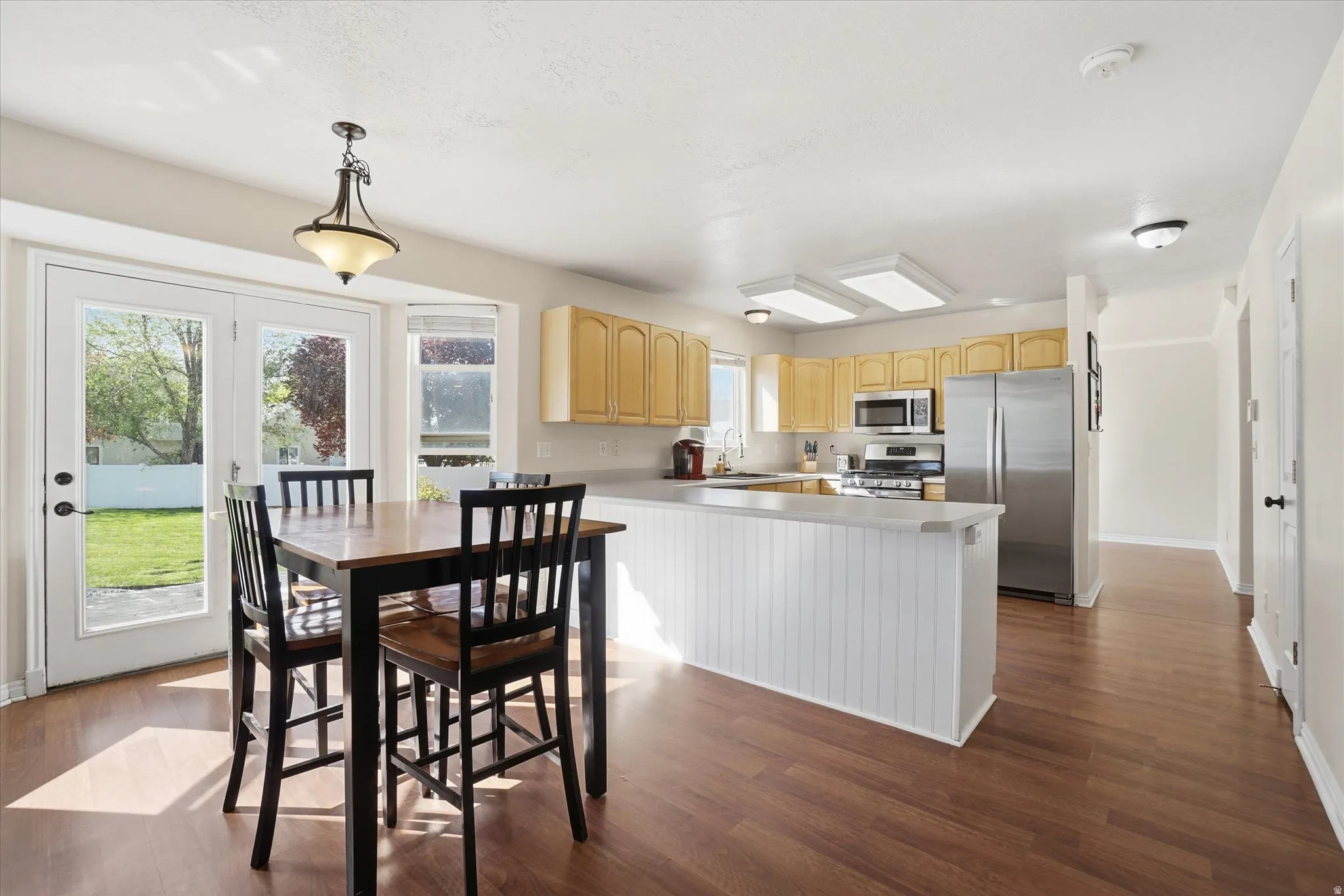 Kitchen with stainless steel appliances, light wood finish cabinetry, light countertops, and dark wood-style floors