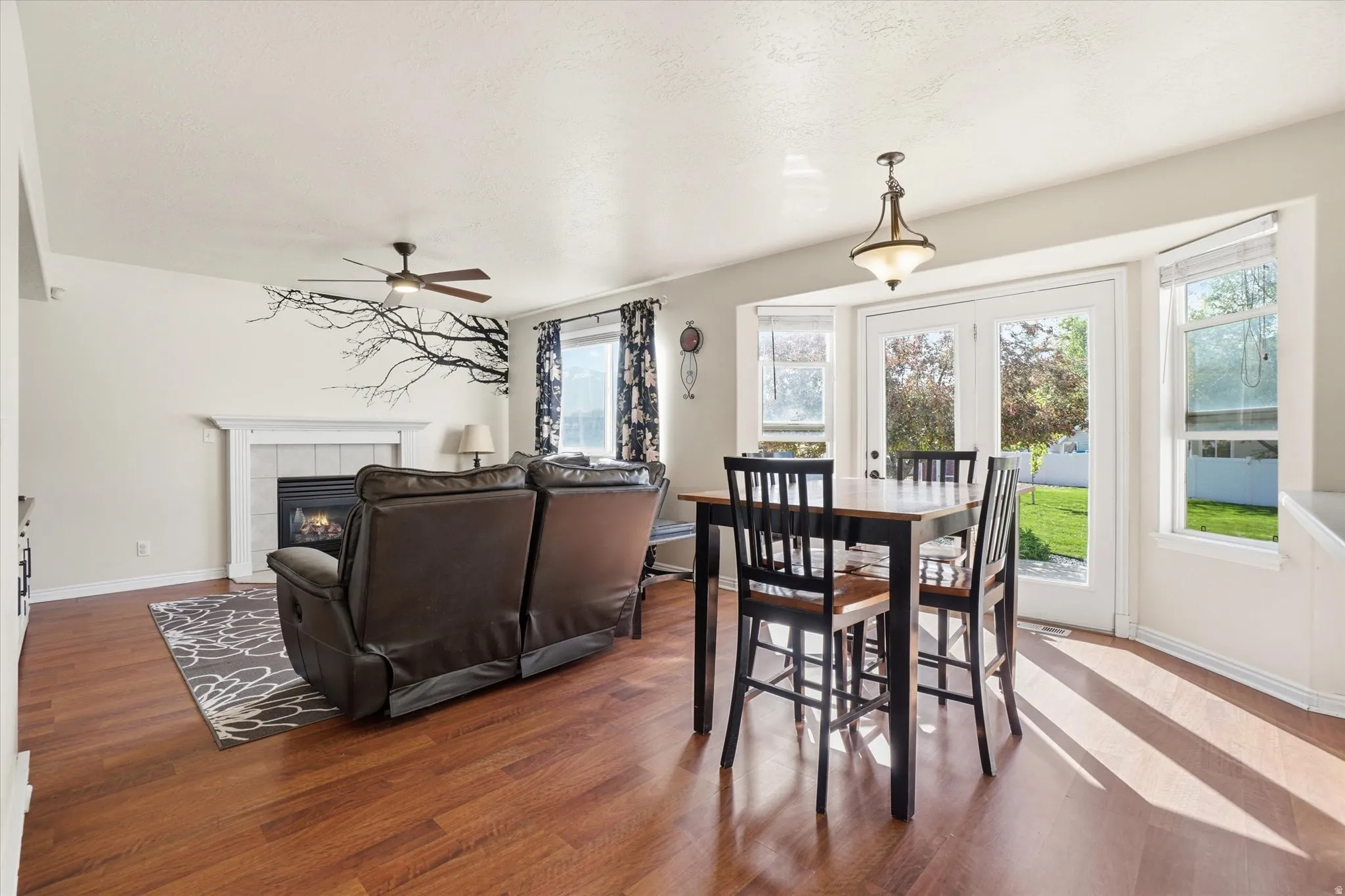 Dining area with wood finished floors, a tile fireplace, and ceiling fan
