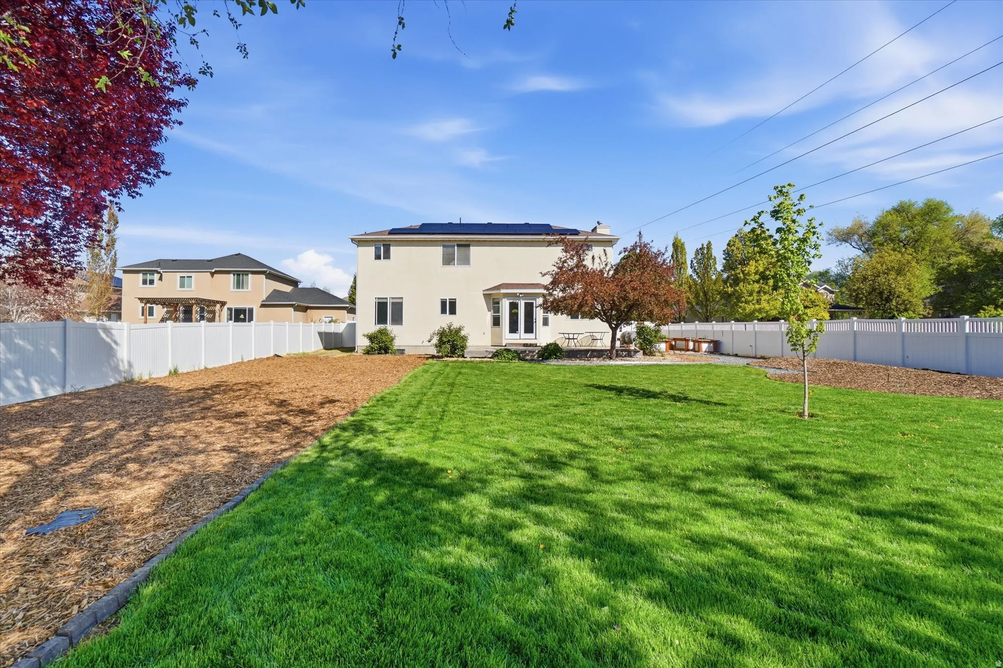 Rear view of house with a fenced backyard, solar panels, and stucco siding