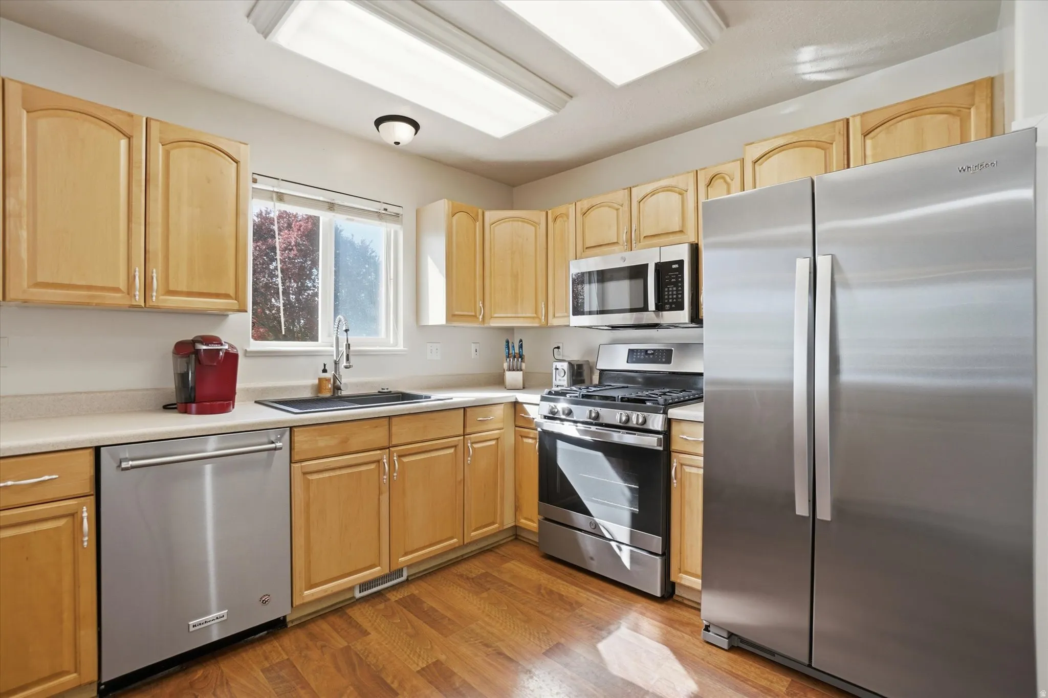 Kitchen with stainless steel appliances, light wood finish cabinetry, light countertops, and dark wood-style floors