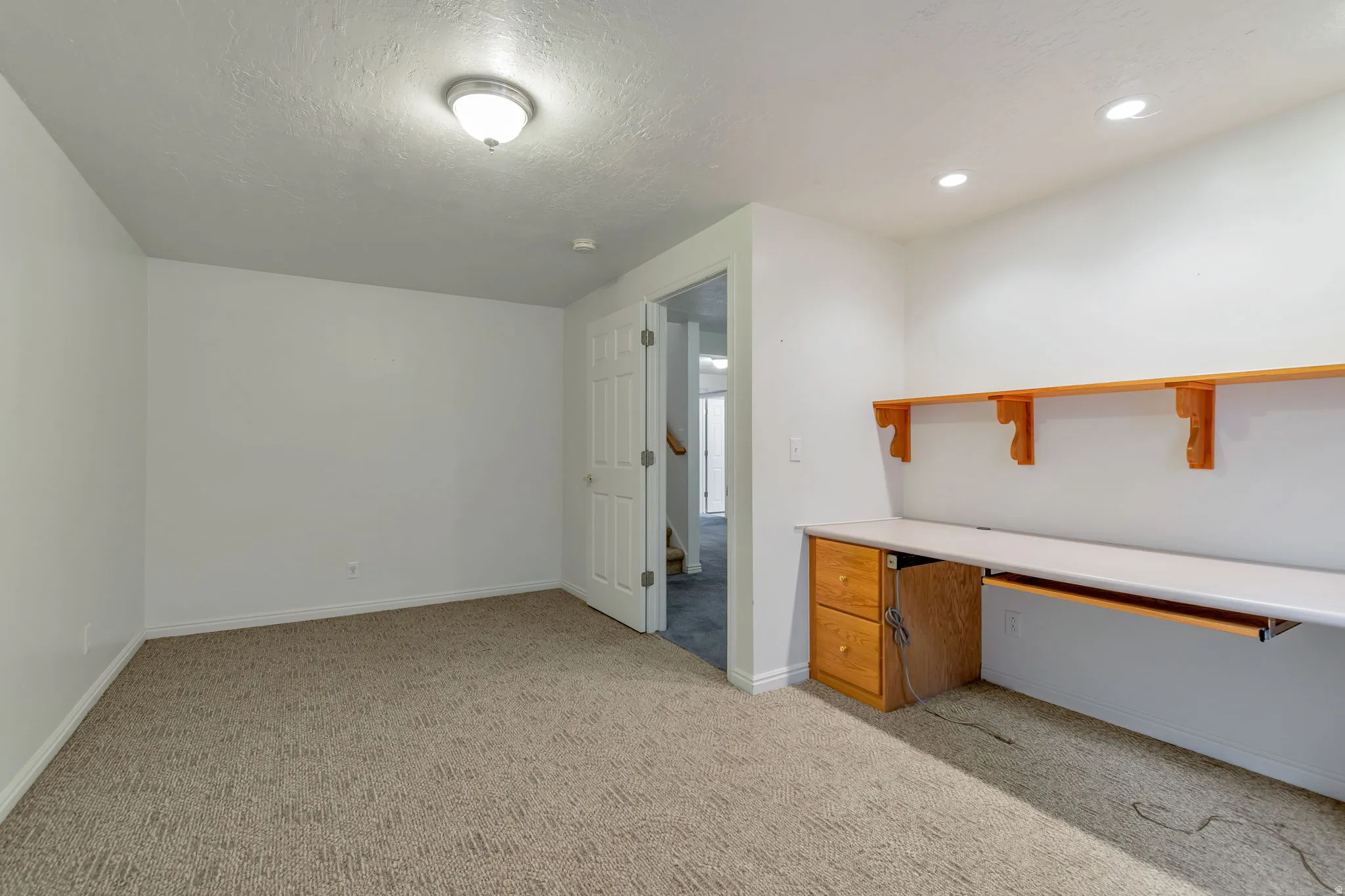 Unfurnished office featuring light colored carpet, built in desk, and a textured ceiling