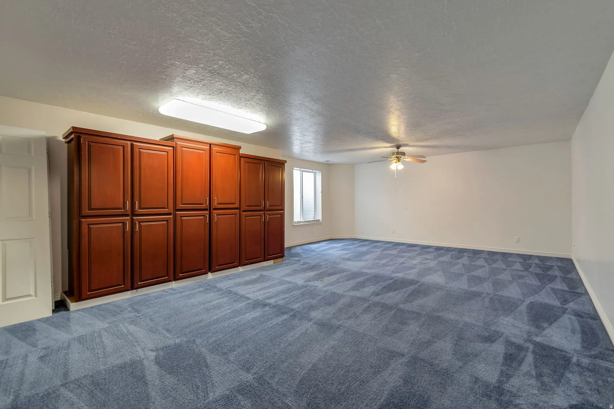 Unfurnished living room with a ceiling fan, a textured ceiling, and dark carpet