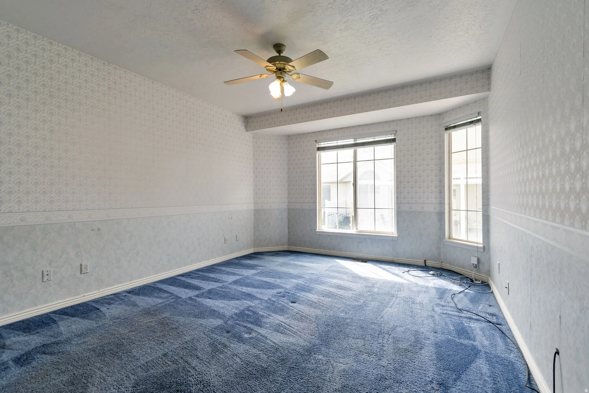 Carpeted spare room featuring wallpapered walls, a textured ceiling, wainscoting, and a ceiling fan
