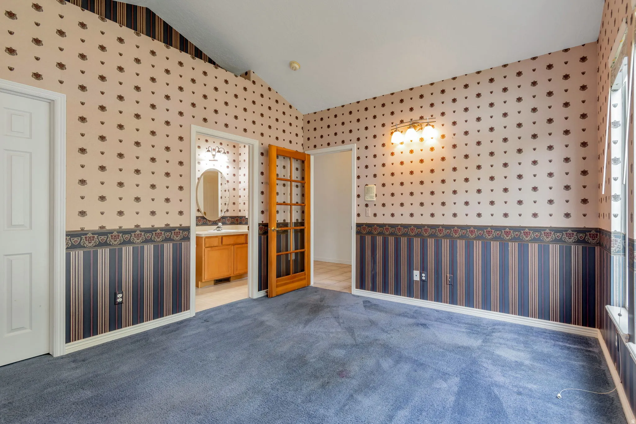 Empty room featuring wallpapered walls, vaulted ceiling, and light carpet