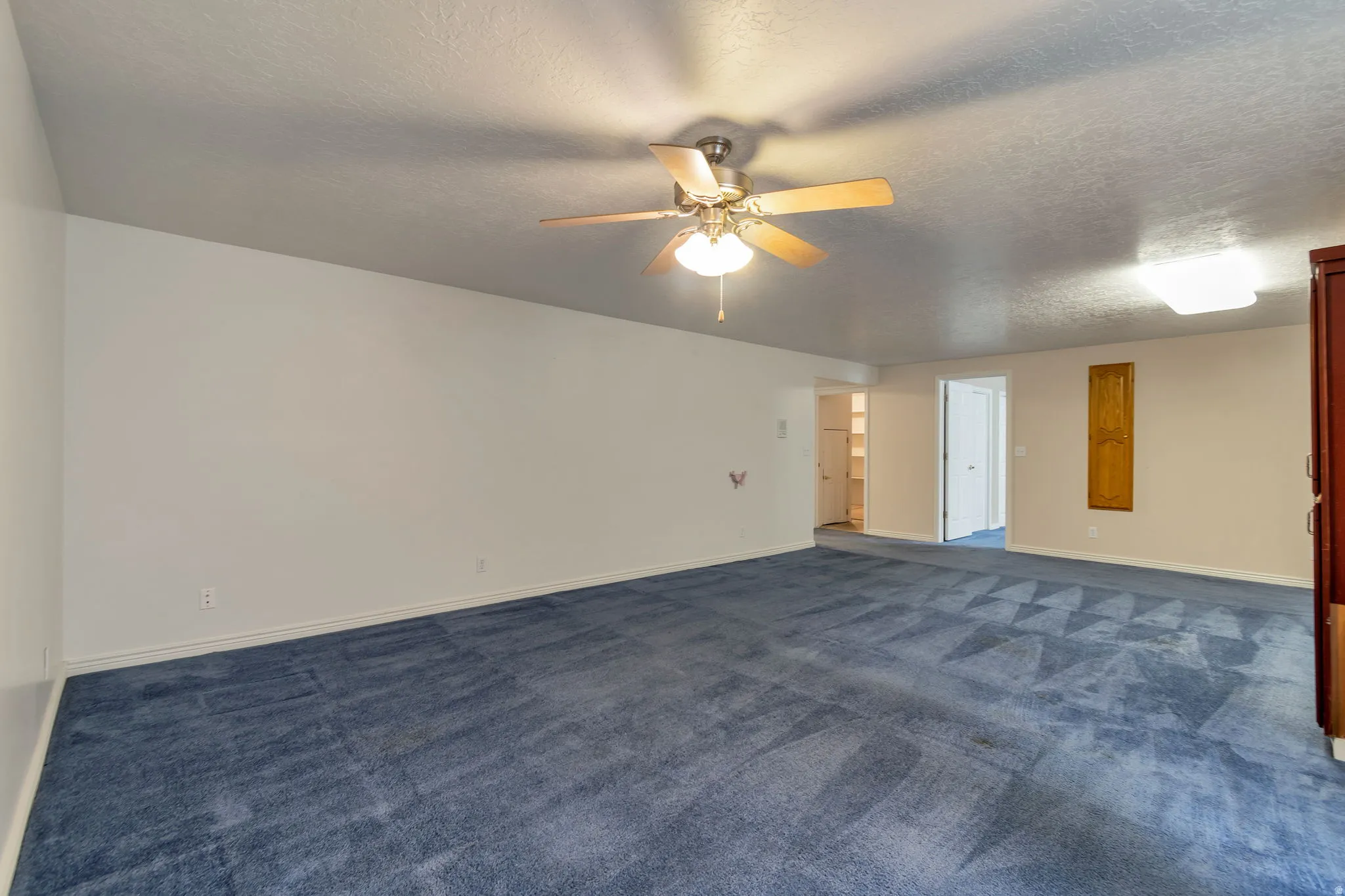 Unfurnished room featuring a textured ceiling, dark carpet, and ceiling fan