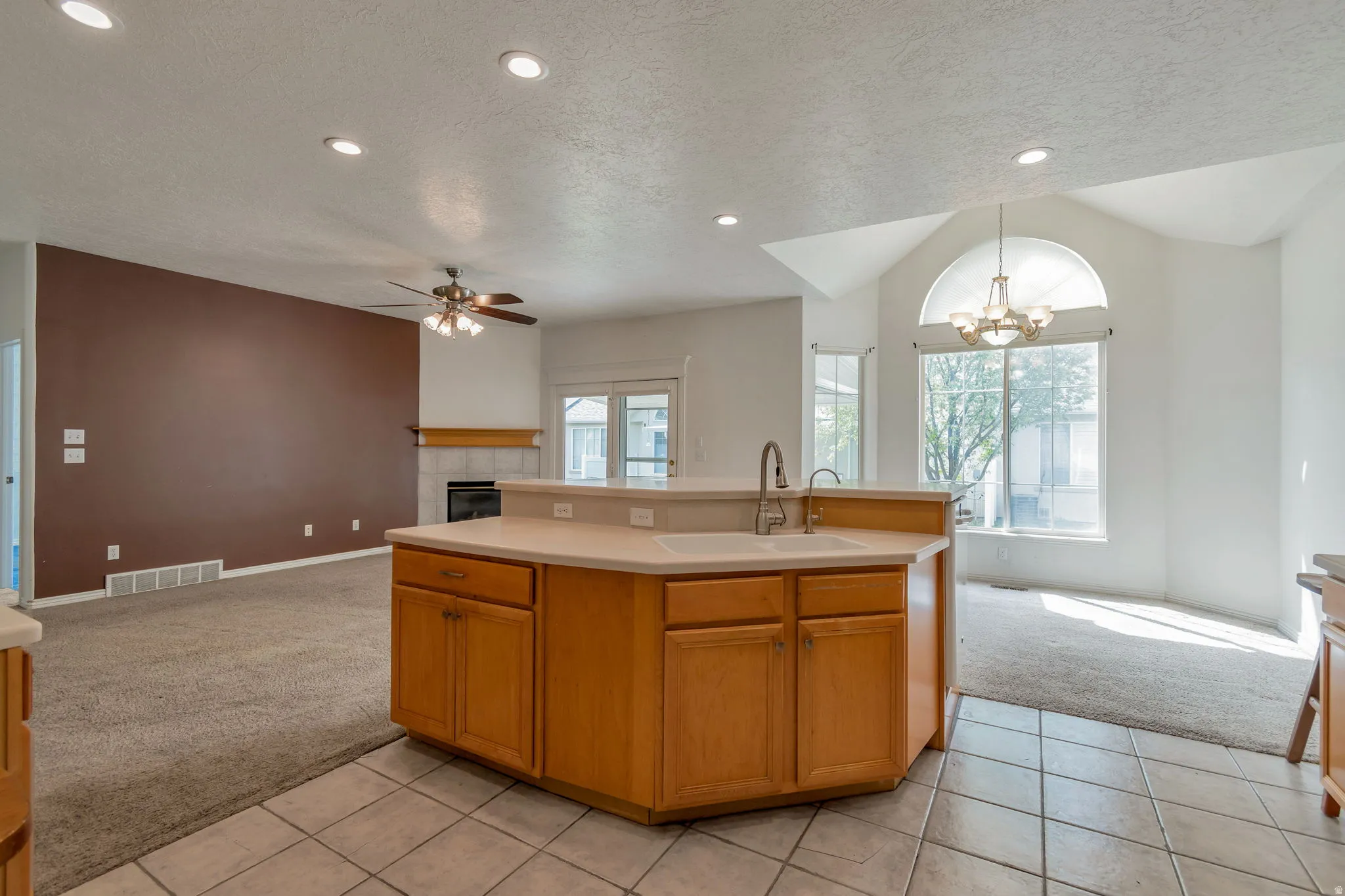 Kitchen featuring open floor plan, light colored carpet, a textured ceiling, hanging lights, and a kitchen island with sink