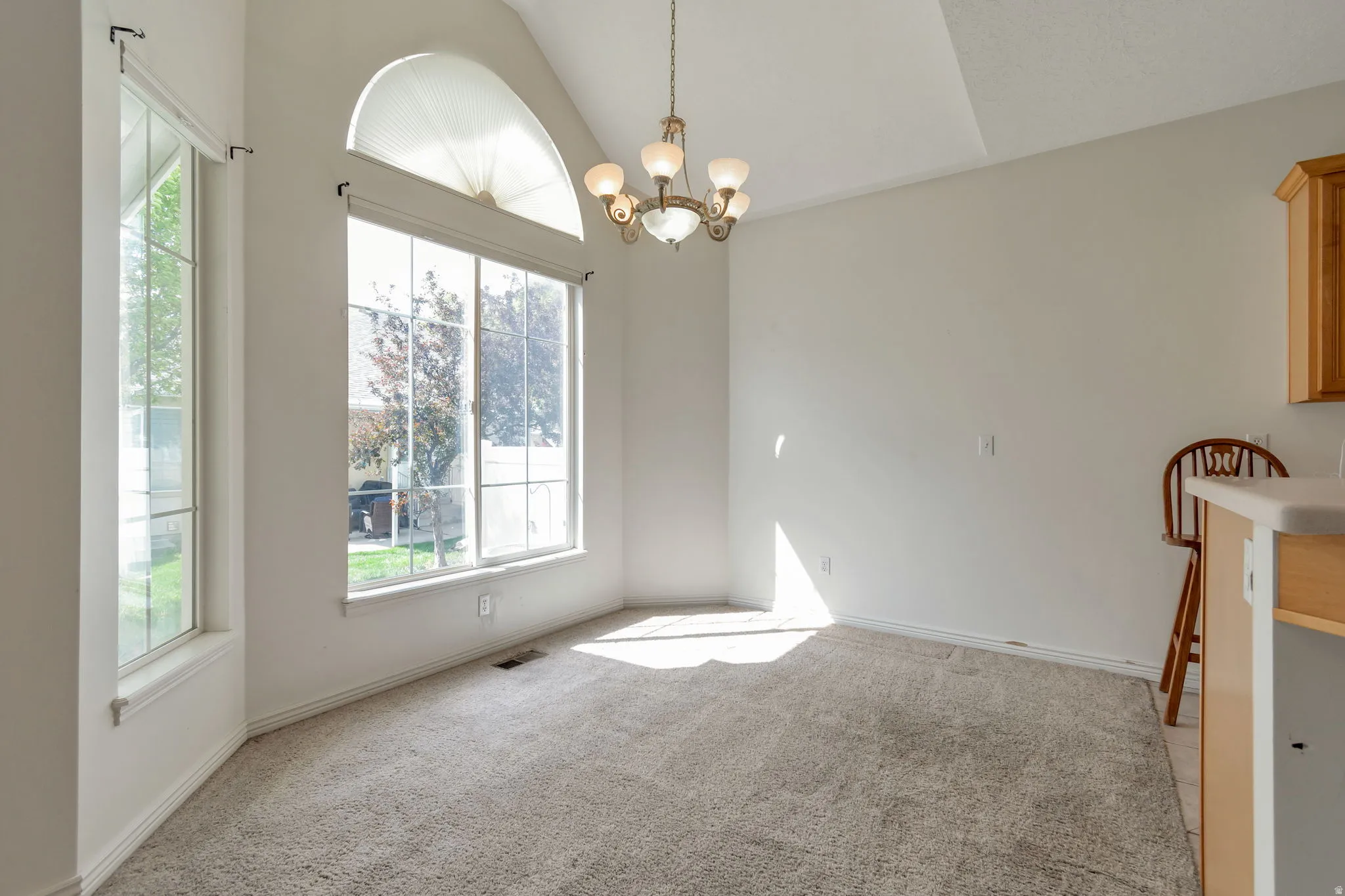 Unfurnished dining area with light carpet, hanging lights, and vaulted ceiling