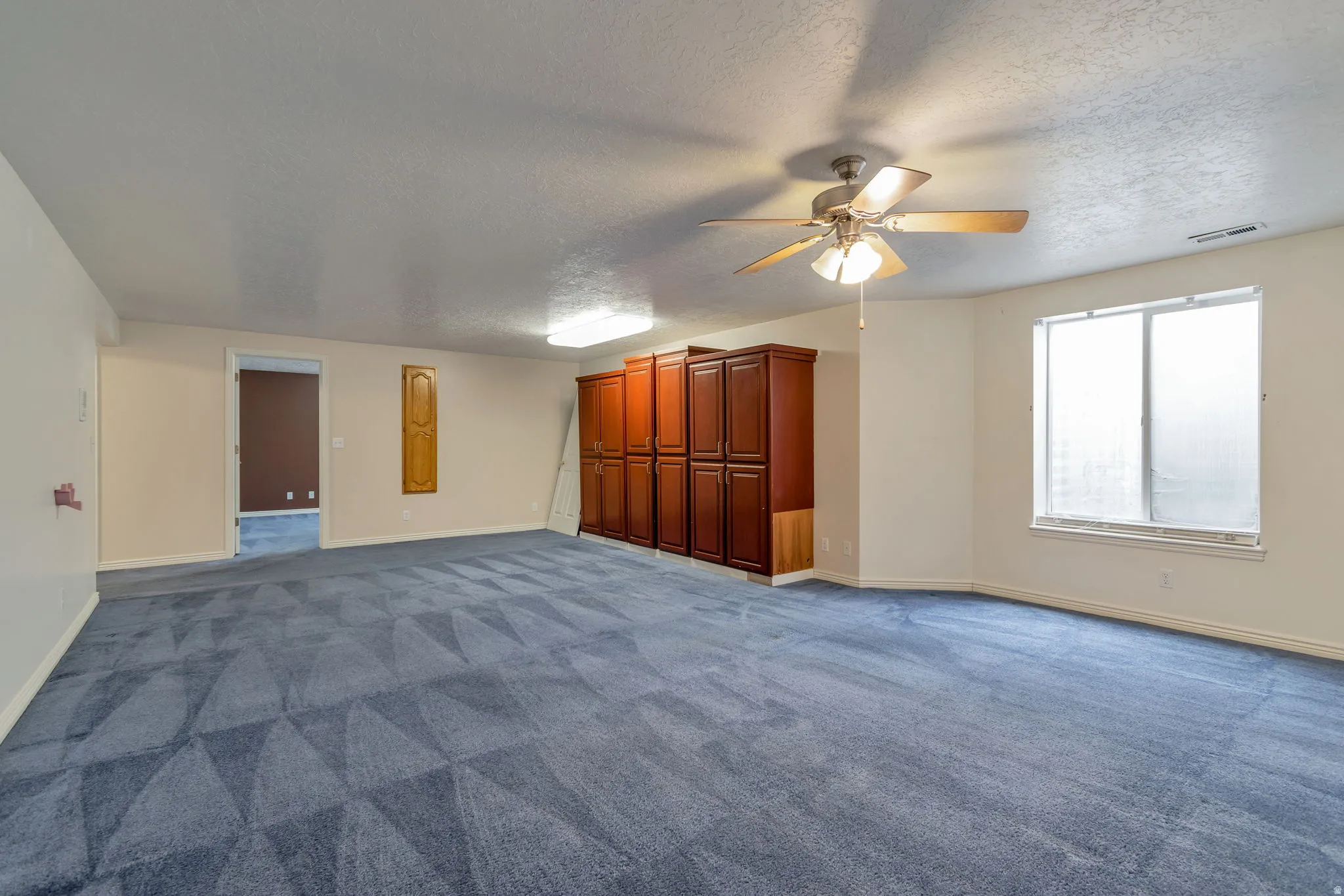 Unfurnished living room featuring dark colored carpet, a textured ceiling, and a ceiling fan