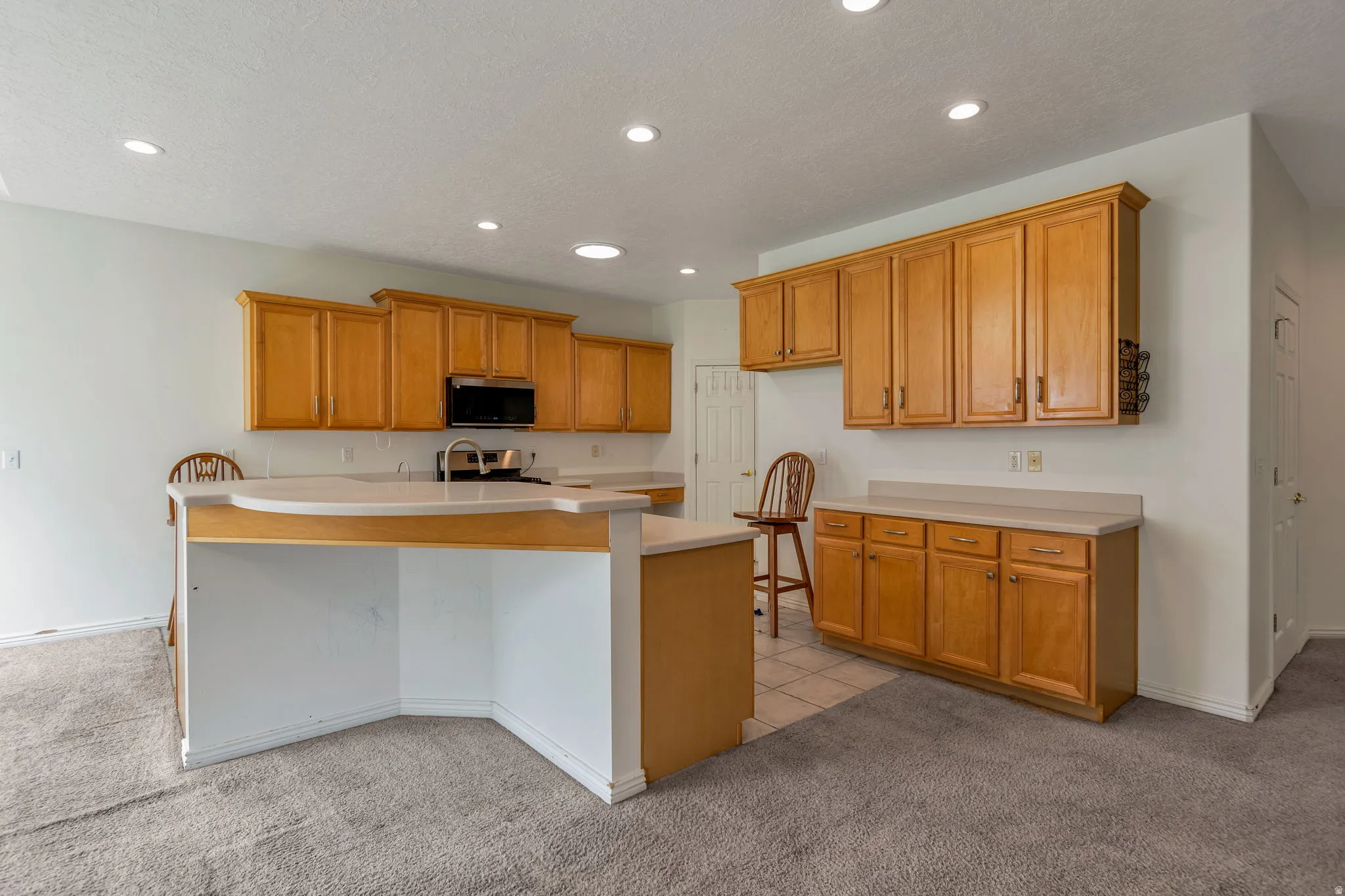 Kitchen with light carpet, light countertops, wood finish cabinets, recessed lighting, and a center island with sink
