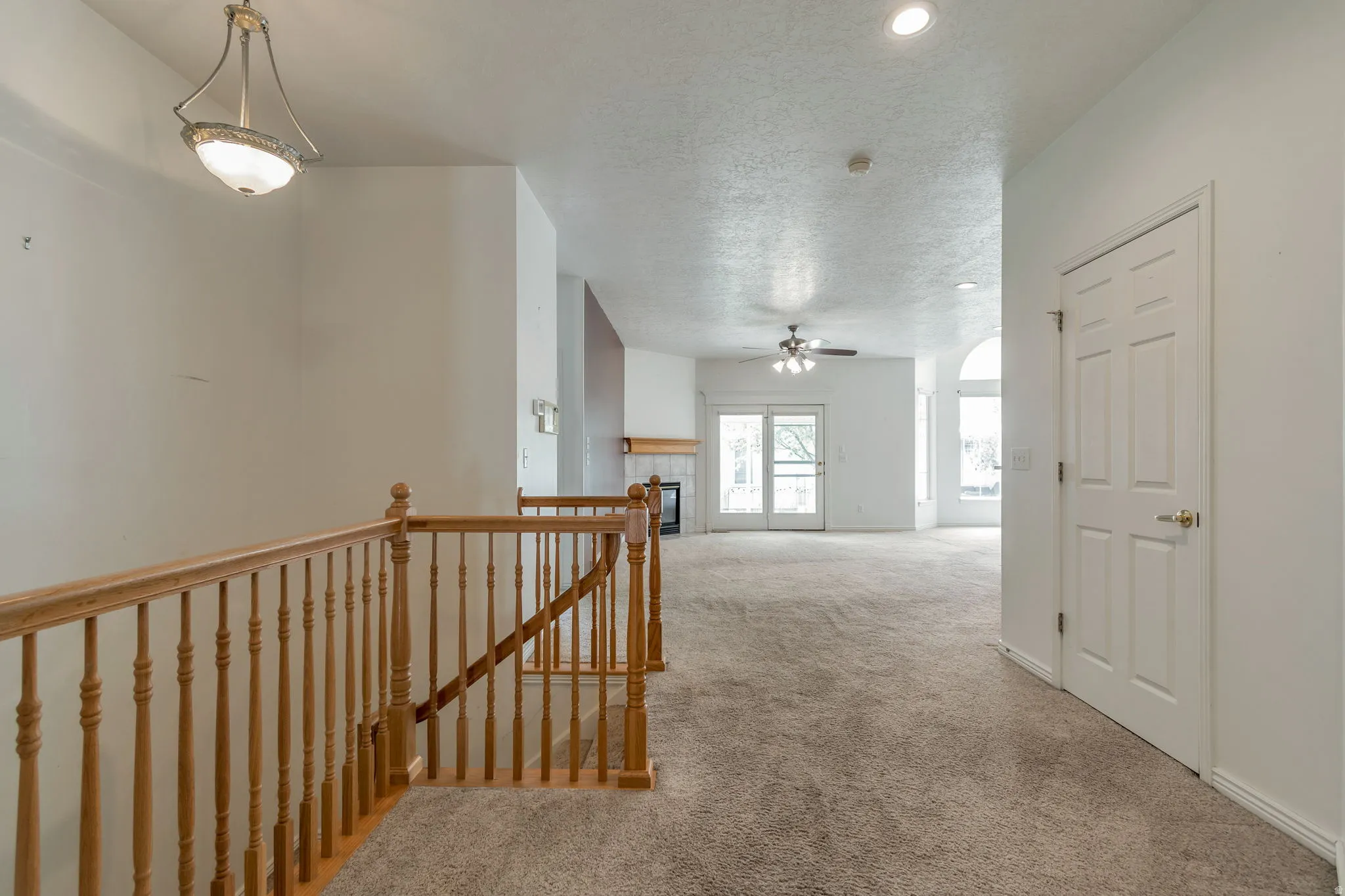 Hallway featuring an upstairs landing, a textured ceiling, light colored carpet, and recessed lighting