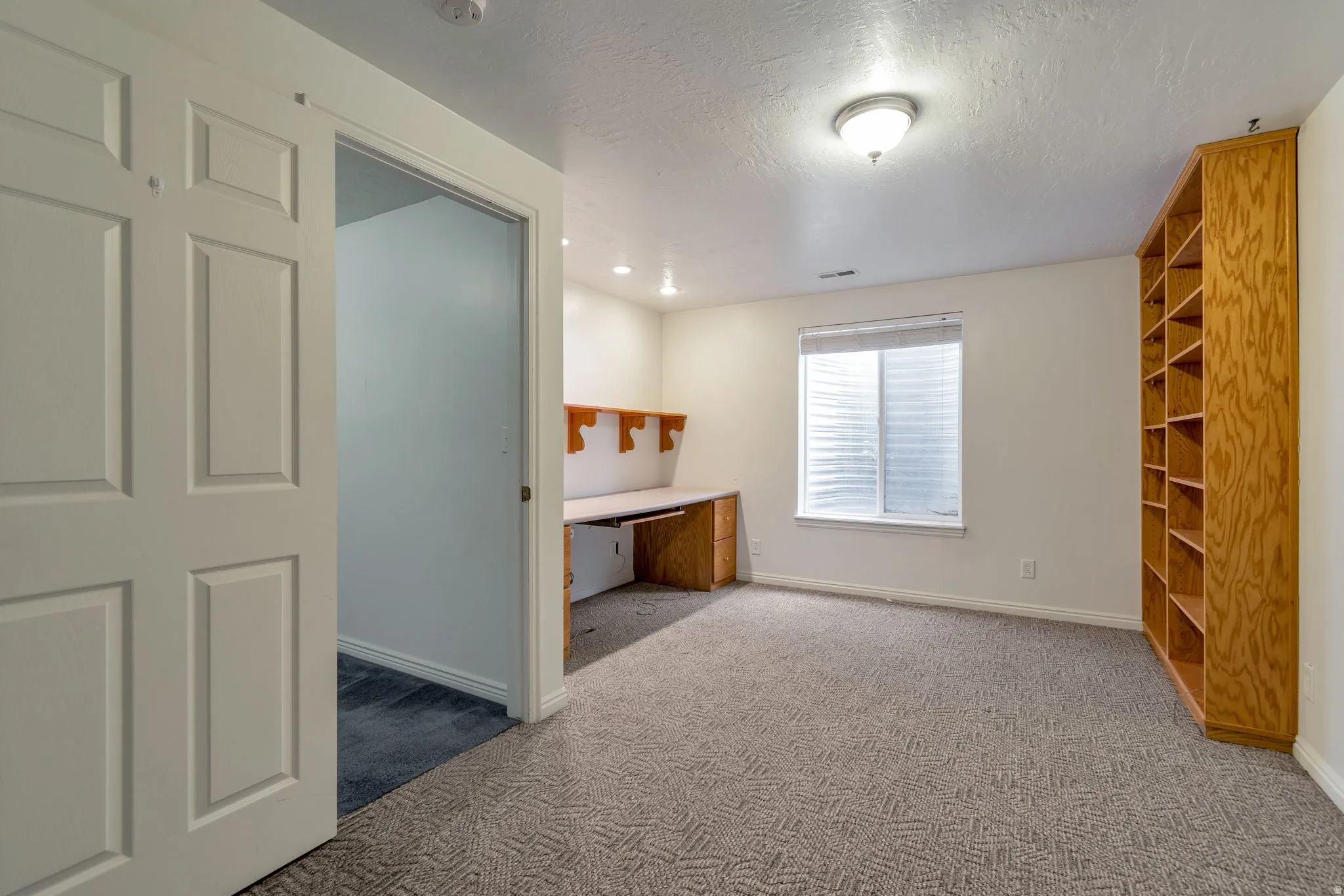 Unfurnished bedroom featuring an office area, carpet flooring, and a textured ceiling
