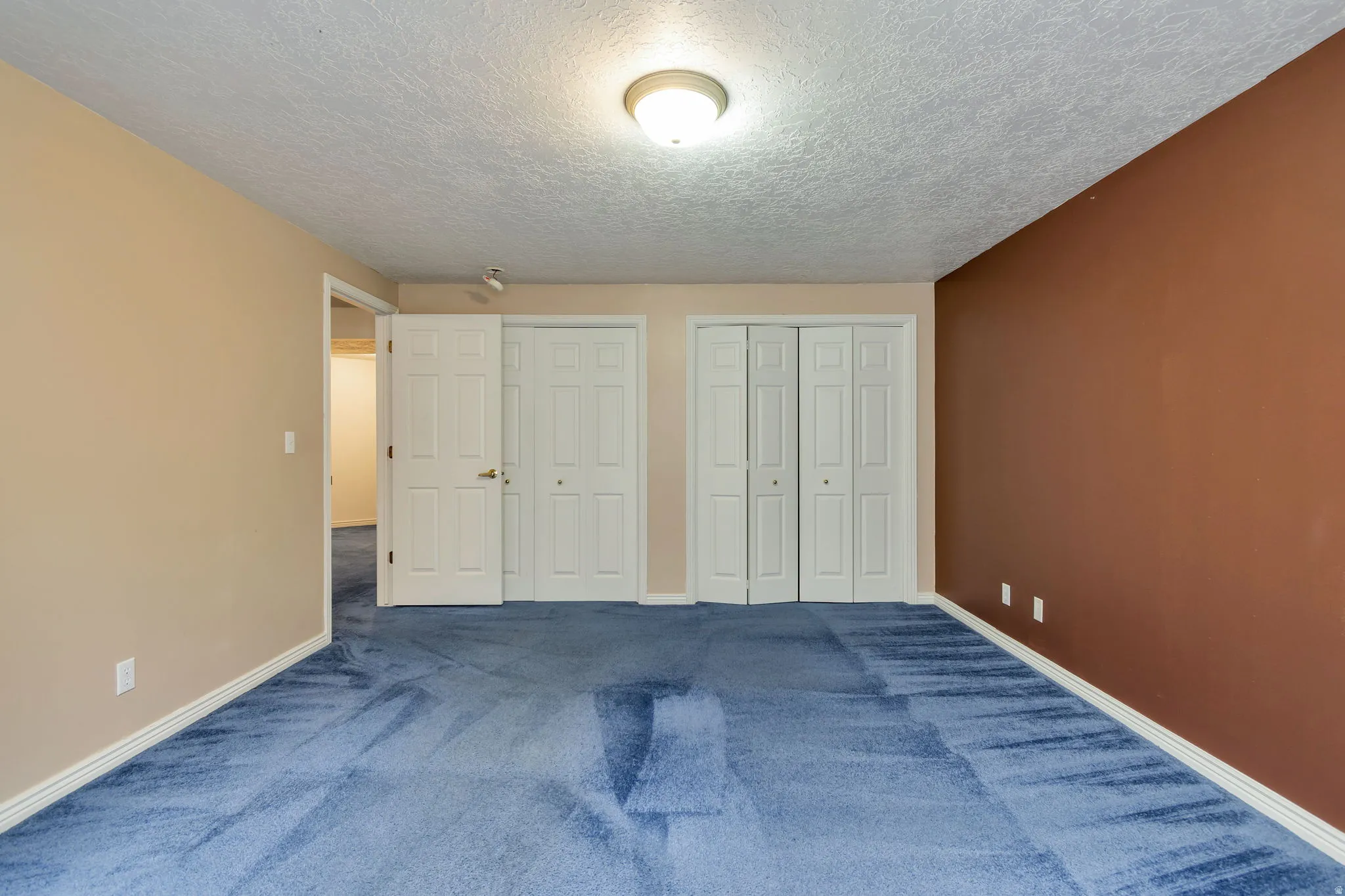 Unfurnished bedroom featuring two closets, dark carpet, and a textured ceiling
