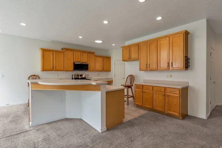 Kitchen with light carpet, light countertops, wood finish cabinets, recessed lighting, and a center island with sink