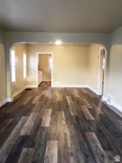 Empty room with arched walkways and dark wood-style floors