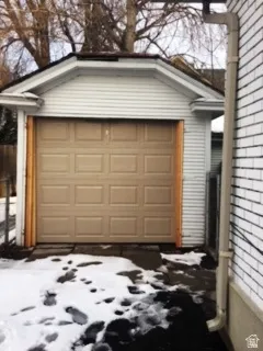 Snow covered garage with concrete driveway