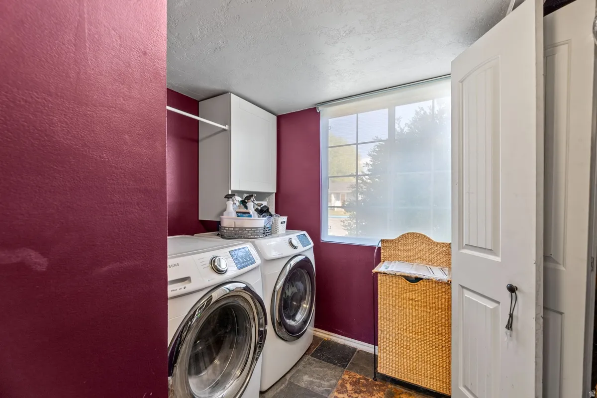 Laundry area featuring a textured ceiling, cabinet space, dark stone finish flooring, and washing machine and clothes dryer