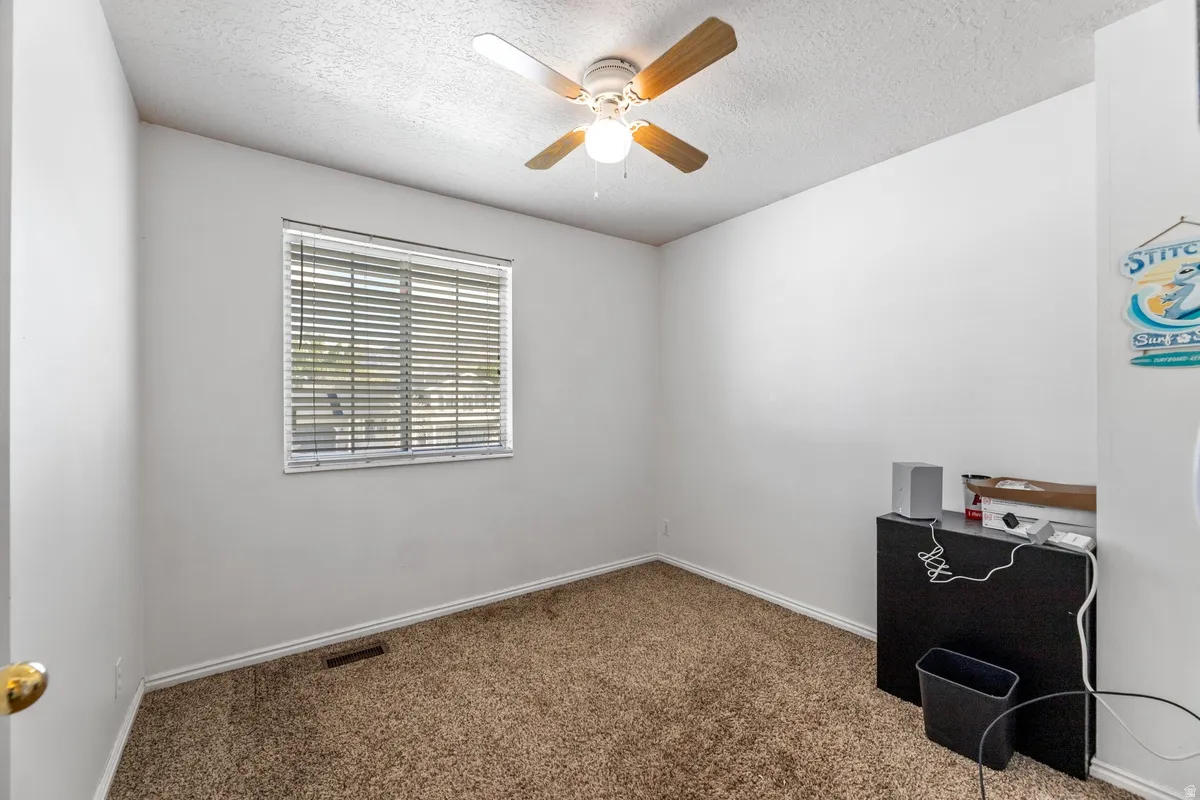 Unfurnished office with dark carpet, a ceiling fan, and a textured ceiling