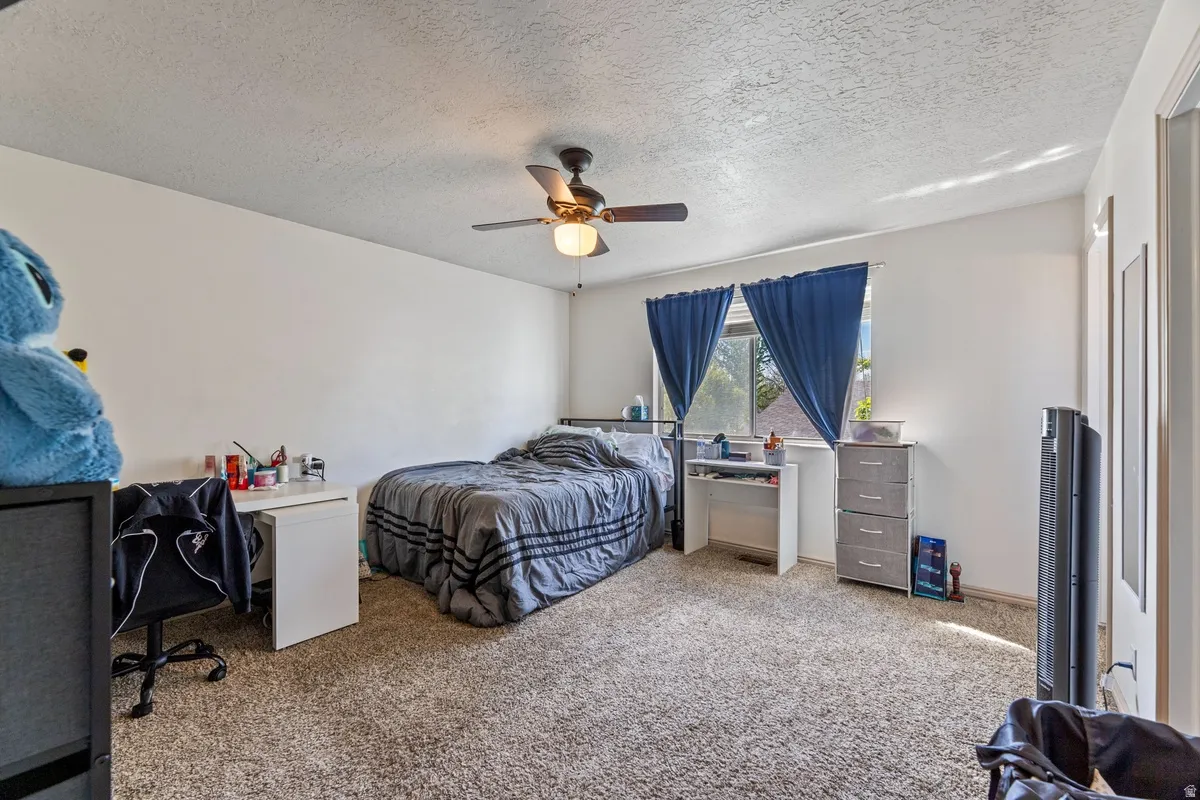 Bedroom with carpet, a textured ceiling, a ceiling fan, and a desk