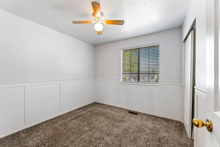 Empty room featuring dark carpet, a decorative wall, ceiling fan, a textured ceiling, and a wainscoted wall