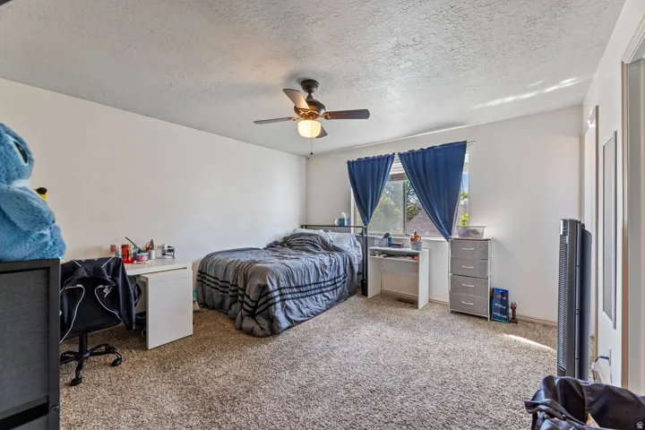 Bedroom with carpet, a textured ceiling, a ceiling fan, and a desk