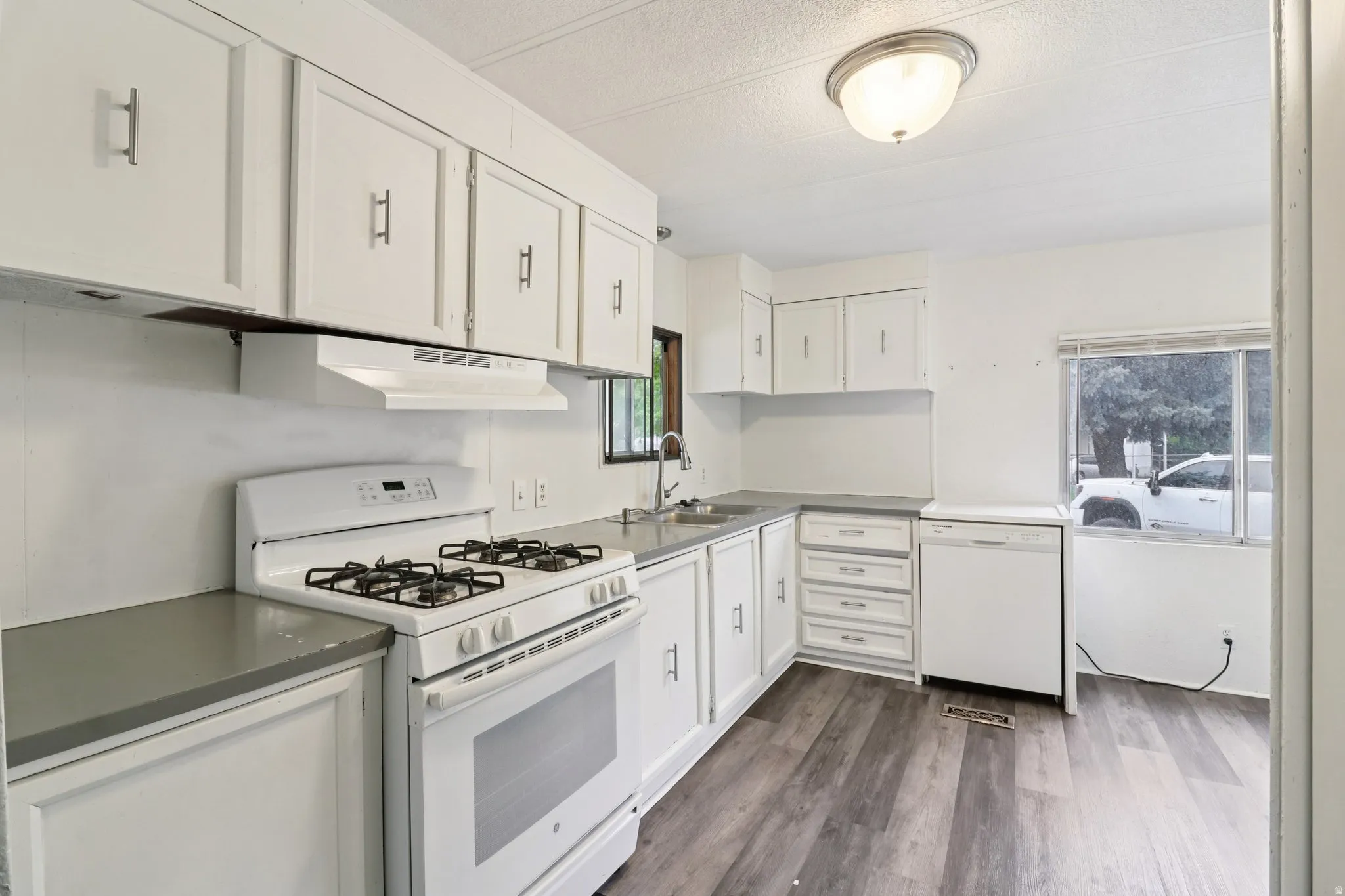 Kitchen featuring white appliances, white cabinets, dark wood-style flooring, and a textured ceiling