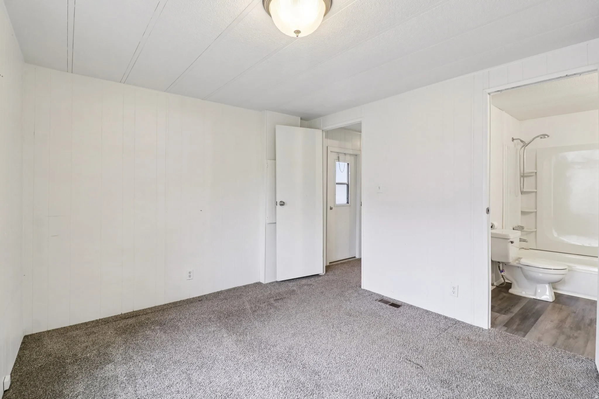 Unfurnished bedroom with carpet floors, ensuite bath, and wood walls
