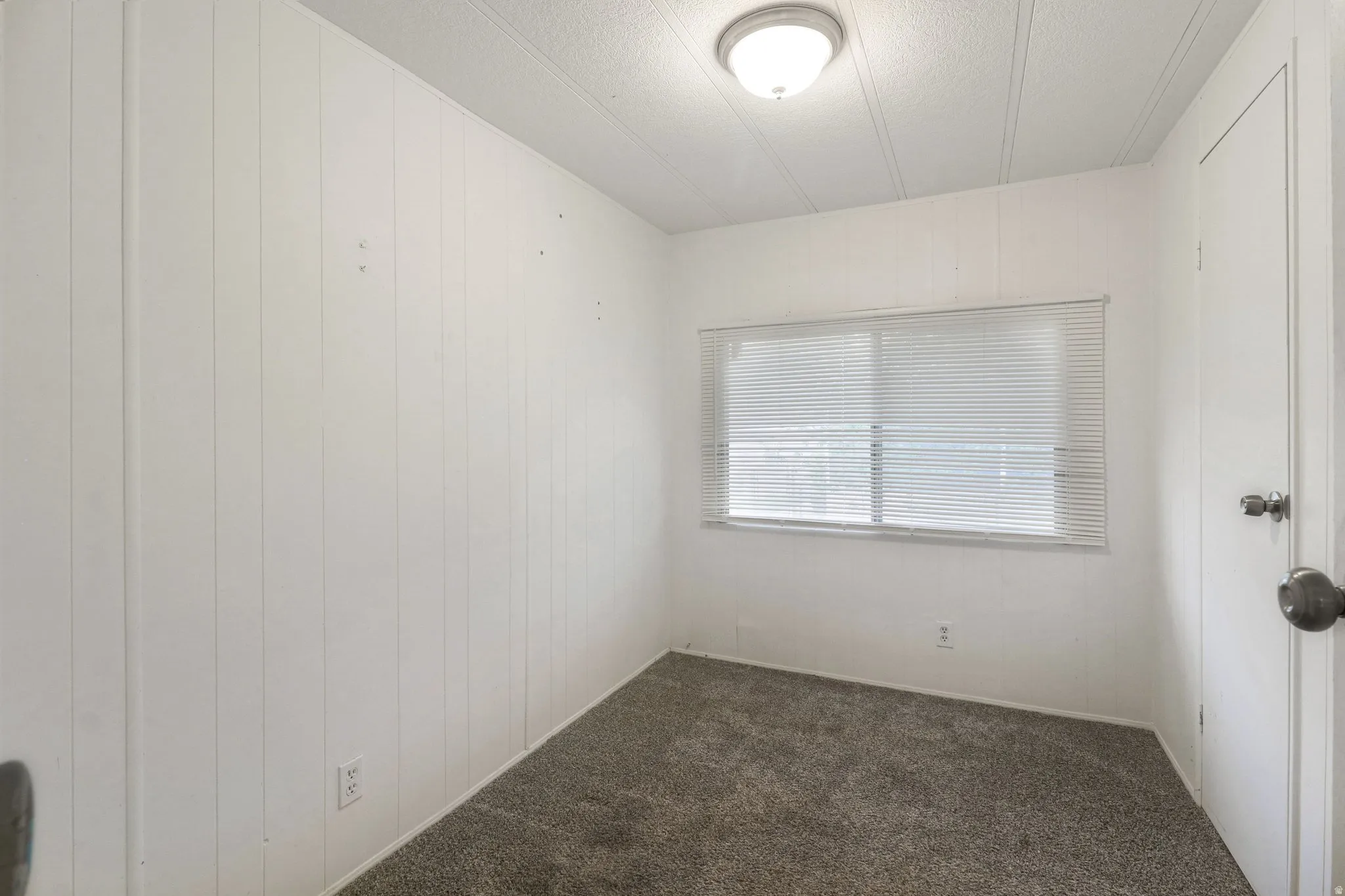 Empty room with dark carpet, wooden walls, and a textured ceiling