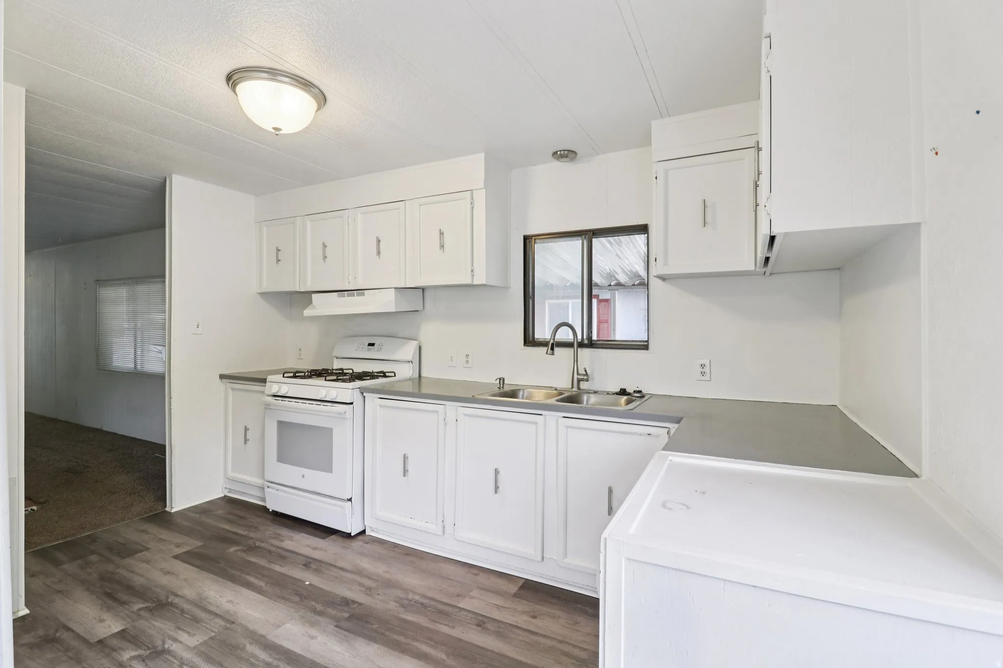 Kitchen featuring white appliances, white cabinetry, dark wood finished floors, and light countertops