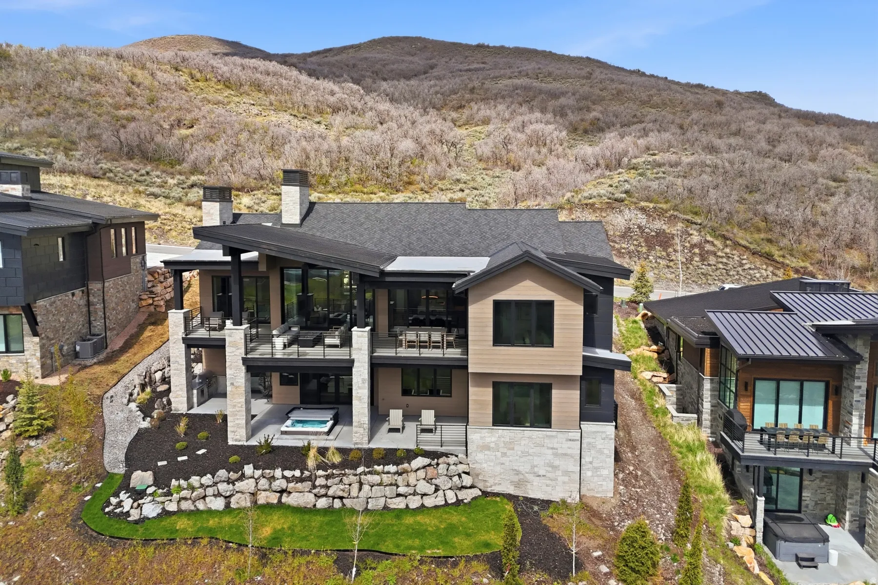 Rear view of property with stone siding, an outdoor hot tub, a mountain view, a chimney, and a patio