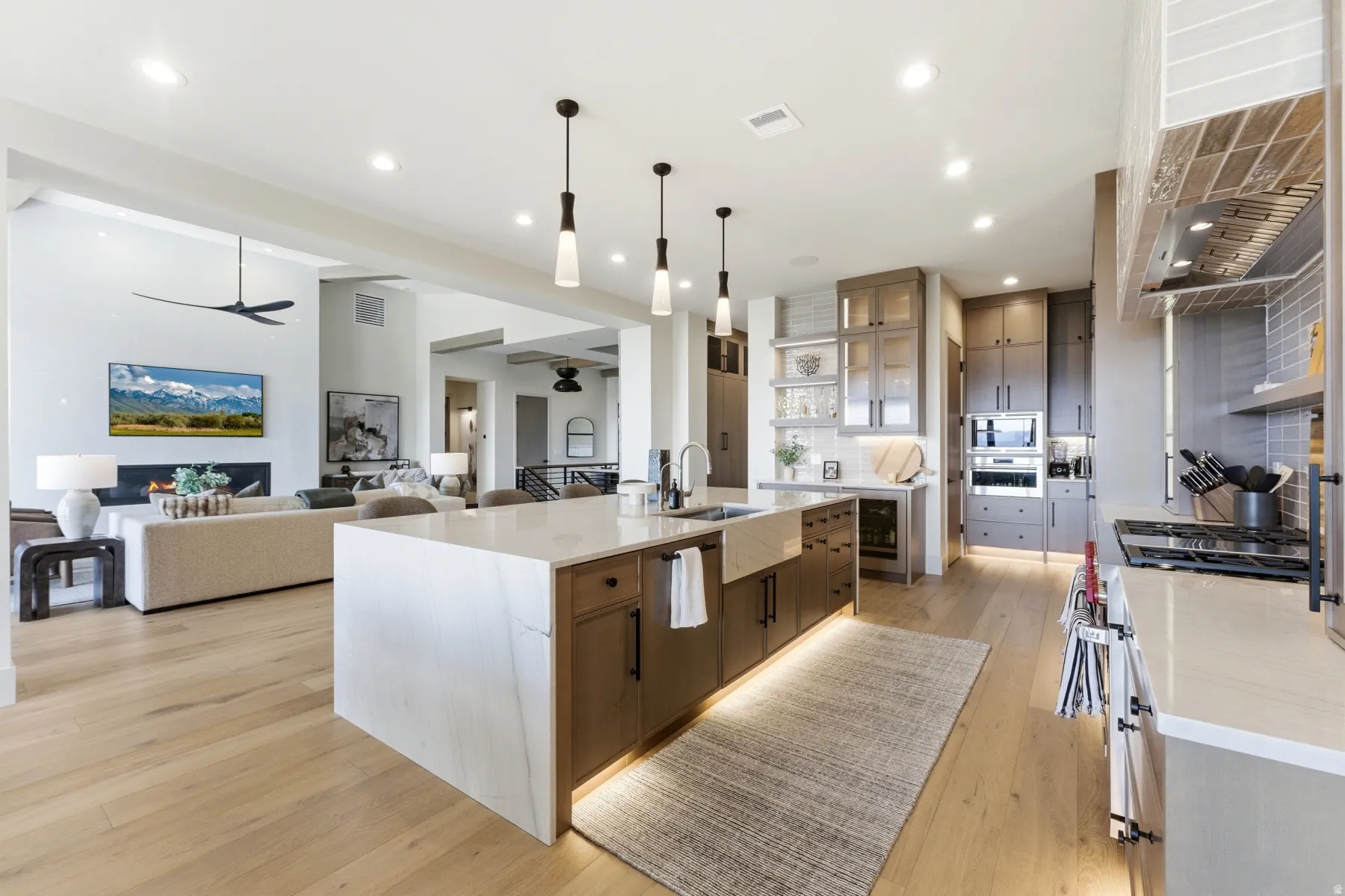Two tone kitchen featuring a ceiling fan, light stone countertops, a large island, two tone cabinetry, and light wood-style flooring