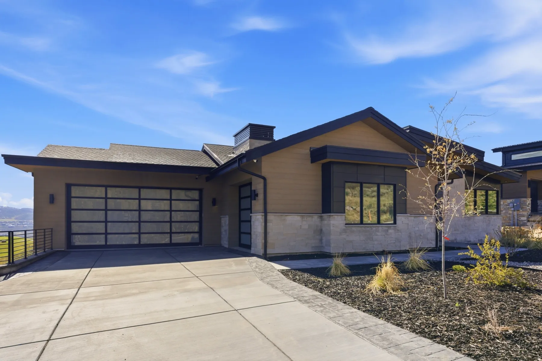 View of front of house featuring an attached garage, concrete driveway, stone siding, and a chimney