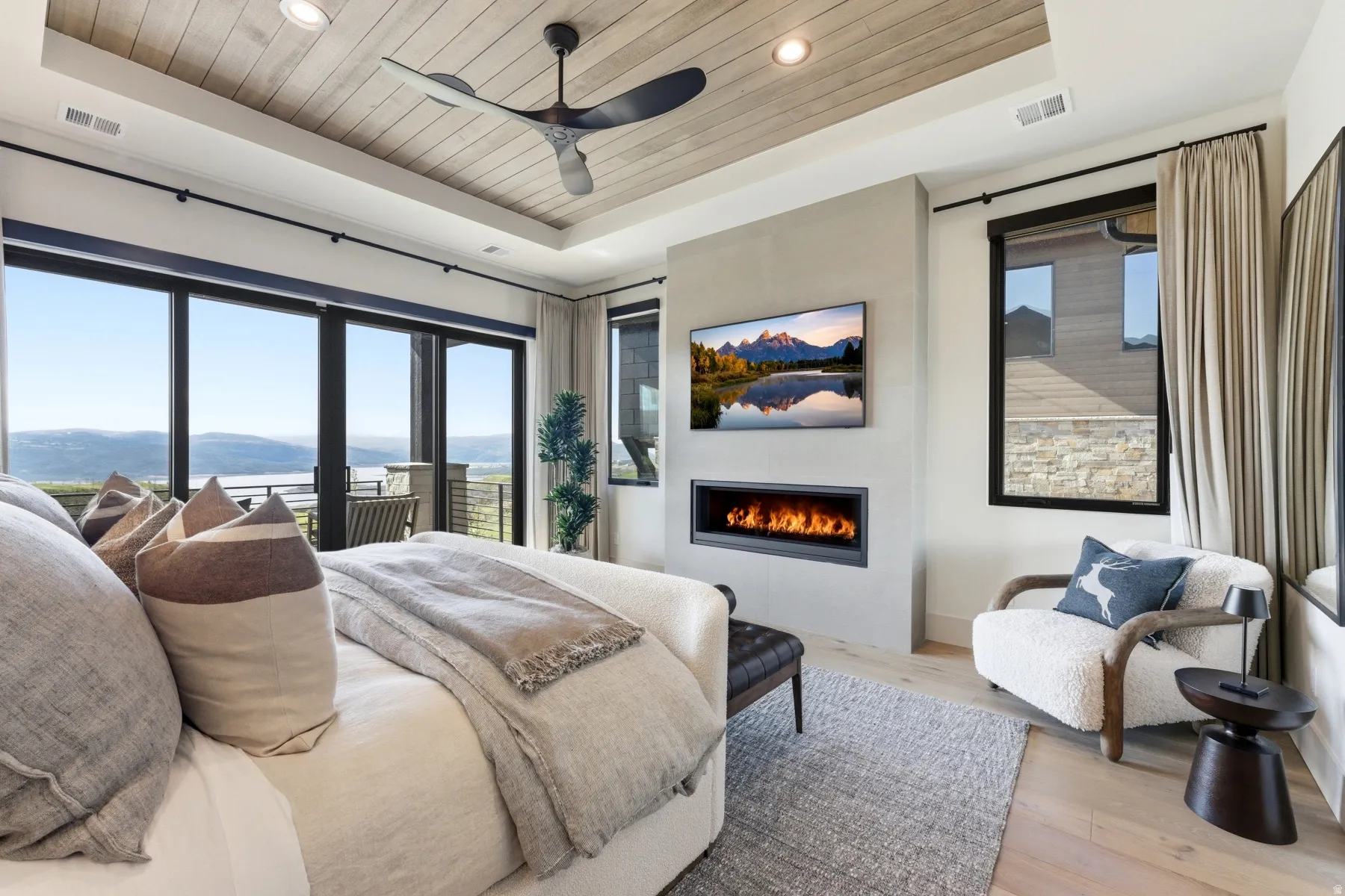 Bedroom with a wood tray ceiling, access to exterior, light wood-style flooring, a large fireplace, and ceiling fan