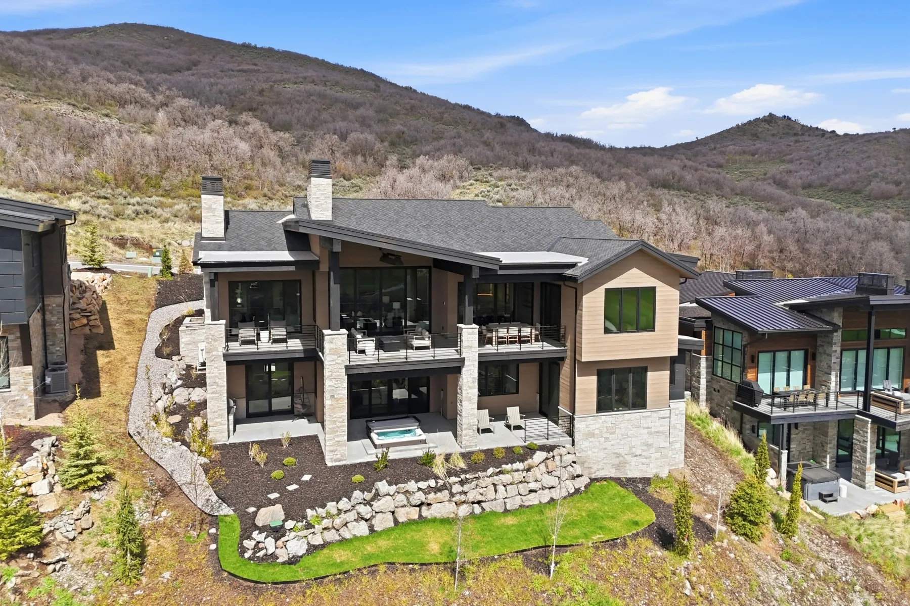 Rear view of property featuring stone siding, a mountain view, a chimney, a patio area, and a jacuzzi