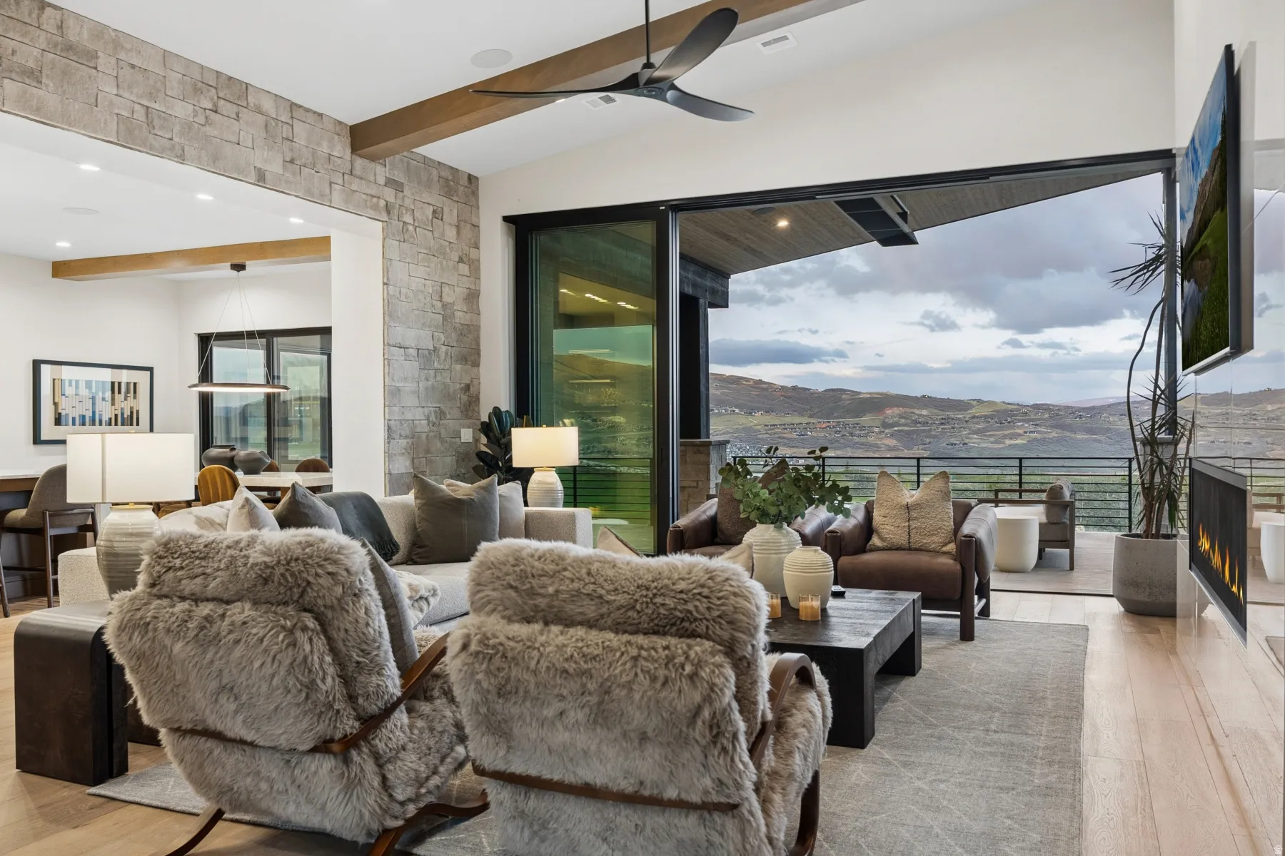 Living area with beamed ceiling, light wood finished floors, ceiling fan, a warm lit fireplace, and recessed lighting